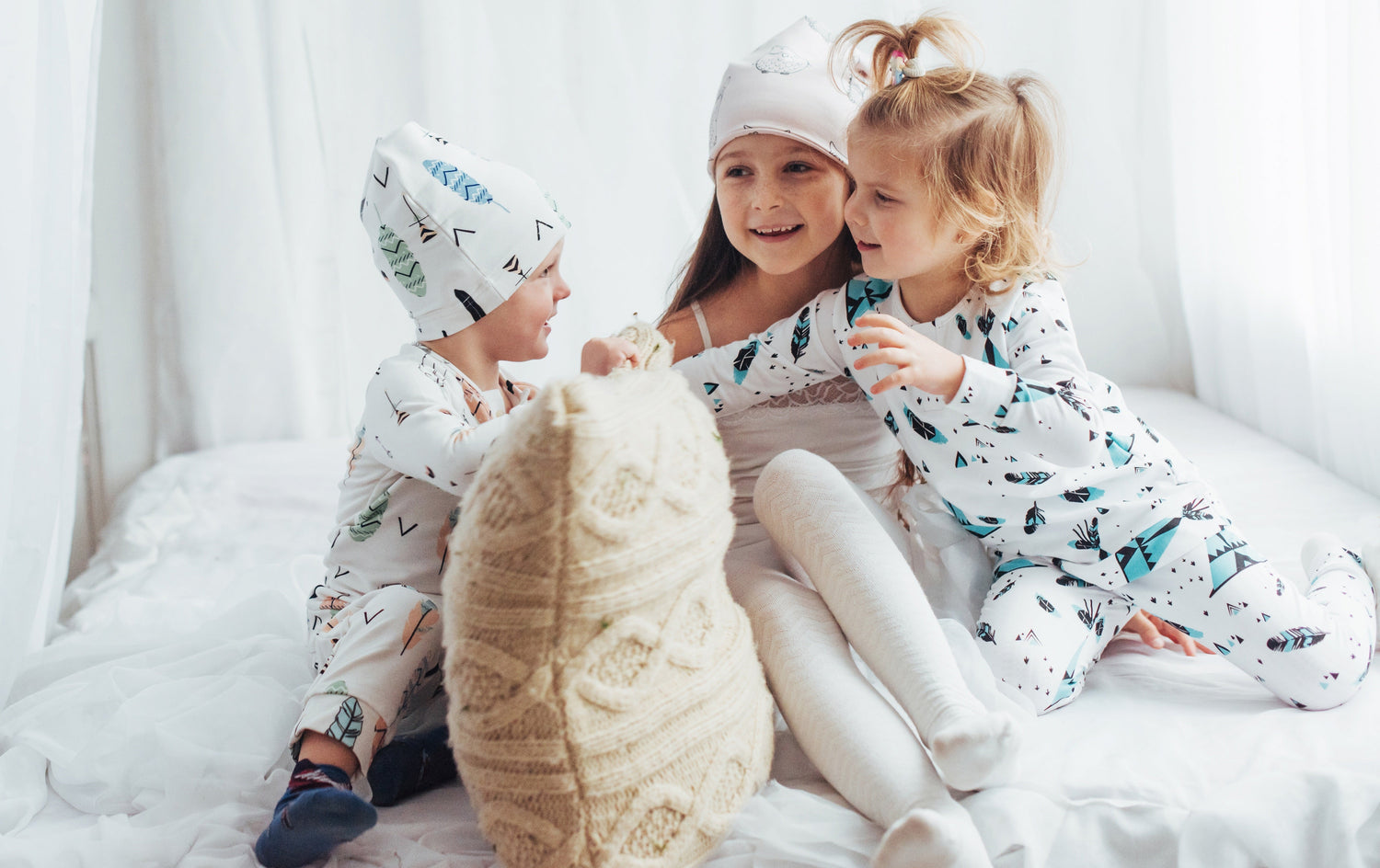 Three kids in cozy pajamas playing on a bed, enjoying comfort and warmth for a good night's sleep.