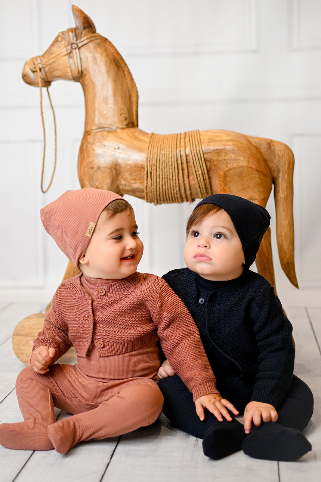 Adorable baby in floral outfit and matching hat, exploring a cozy room with striped pillow.