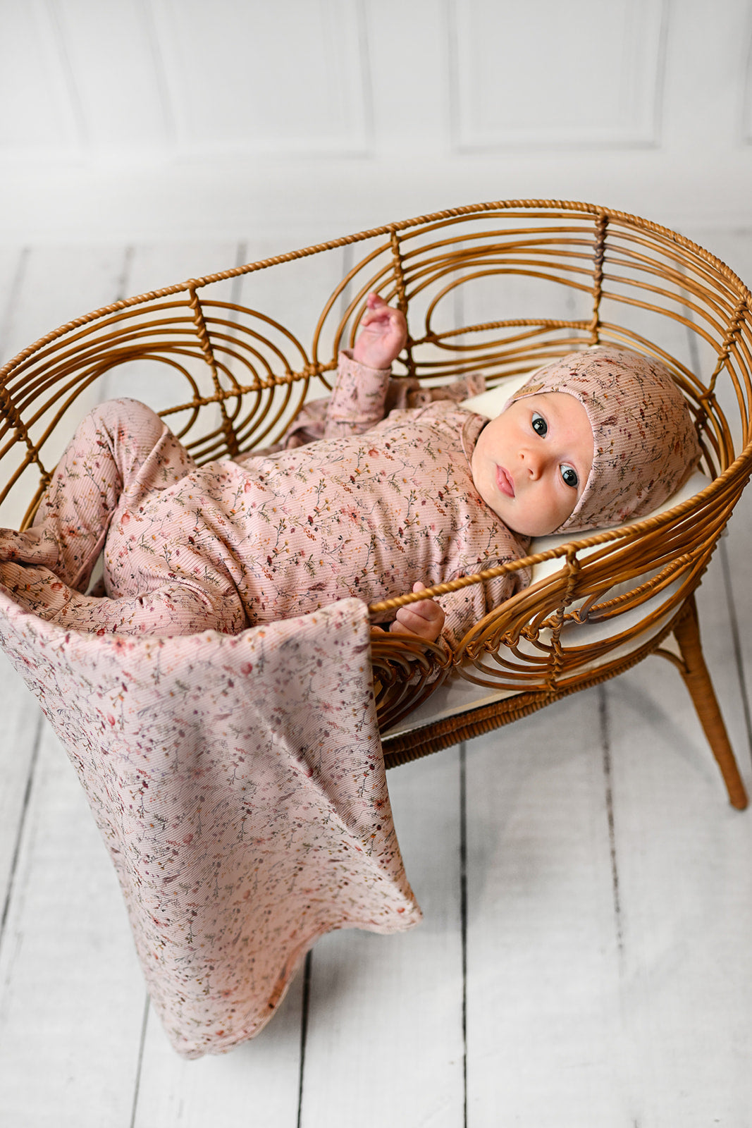 Adorable baby in floral outfit and matching headband, lying on soft blankets in a cozy nursery setting.