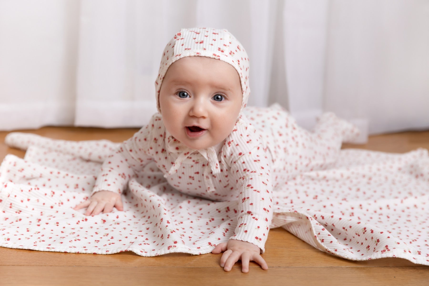 Adorable baby in floral outfit and matching headband, lying on soft blankets in a cozy nursery setting.