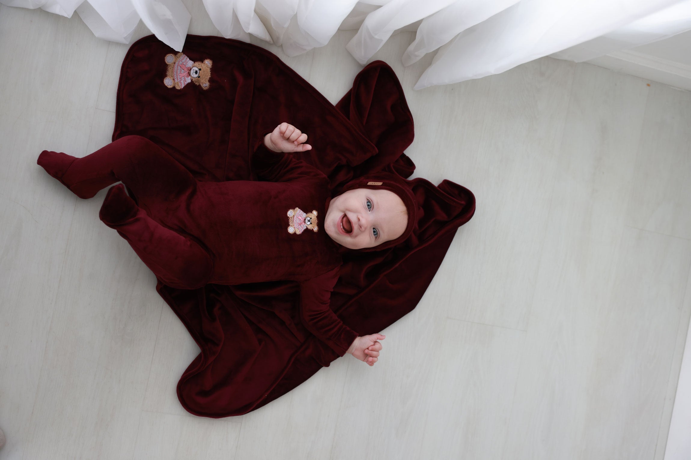 Adorable baby in floral outfit and matching headband, lying on soft blankets in a cozy nursery setting.