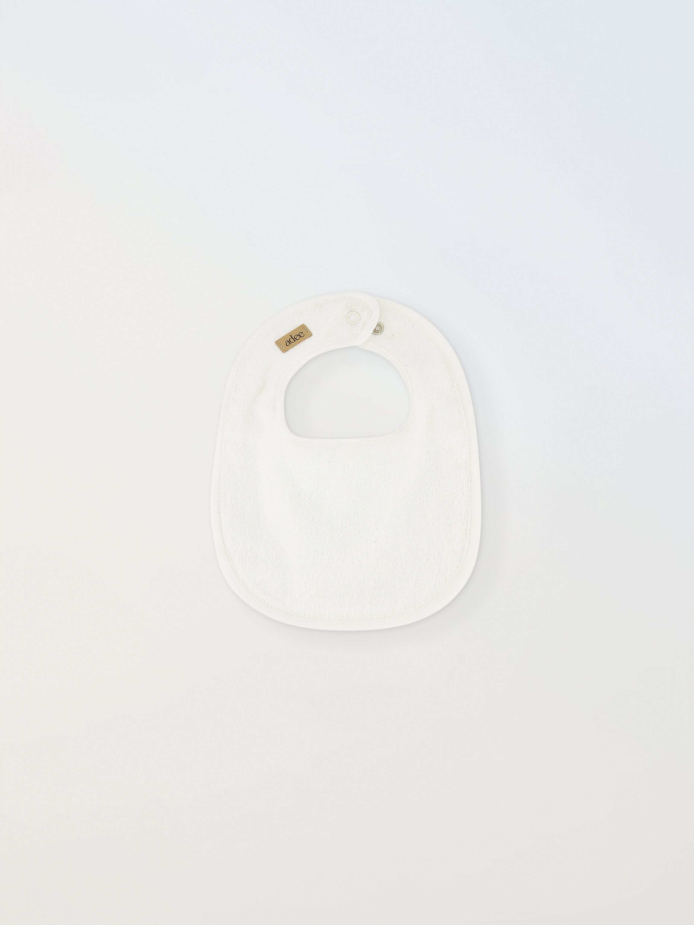 Small white Adee bib for infants; unisex with brown Adee label.
