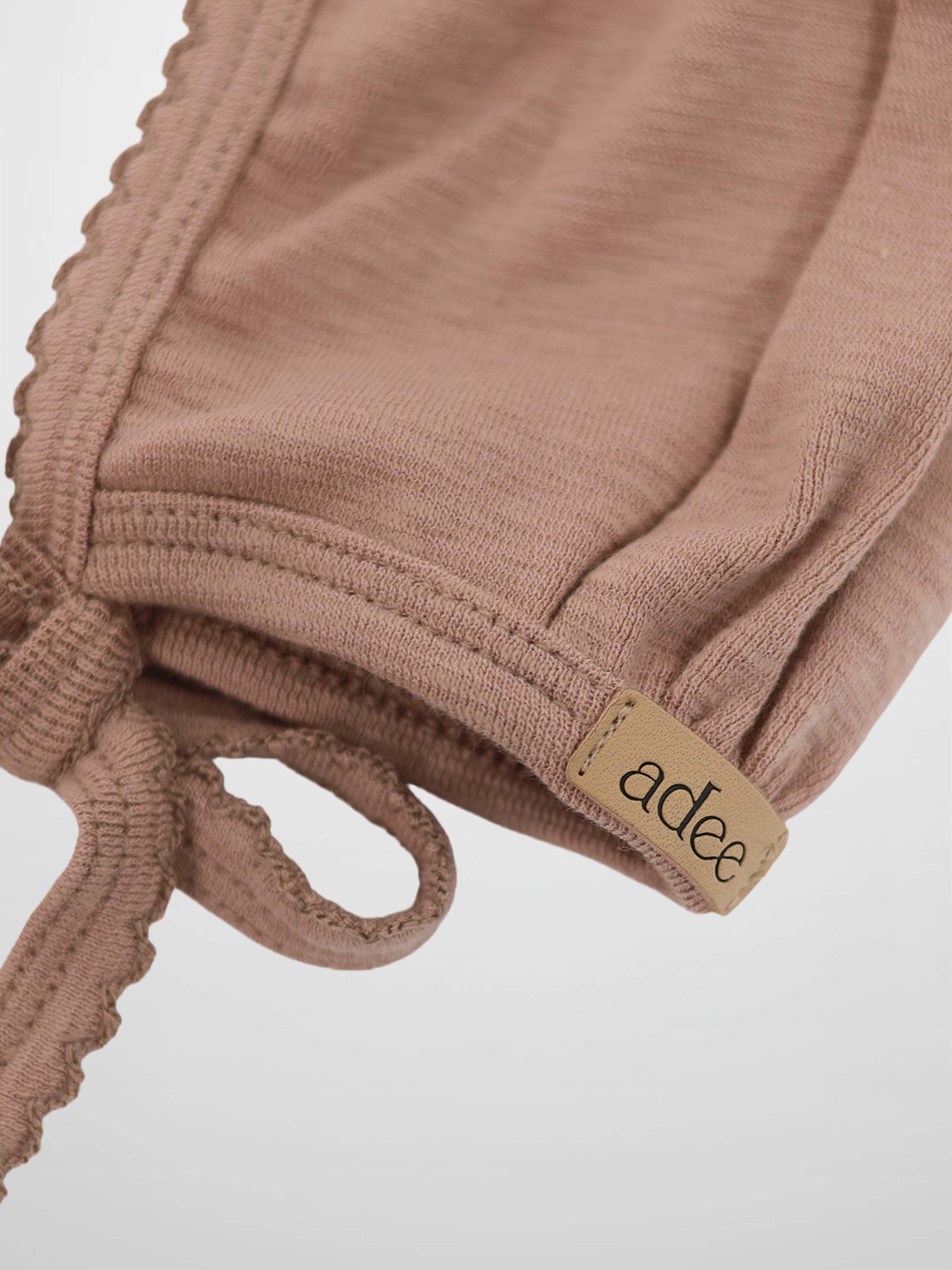 Pink scalloped bonnet for girls, dusty pink knit with ties and Adee brand tag.