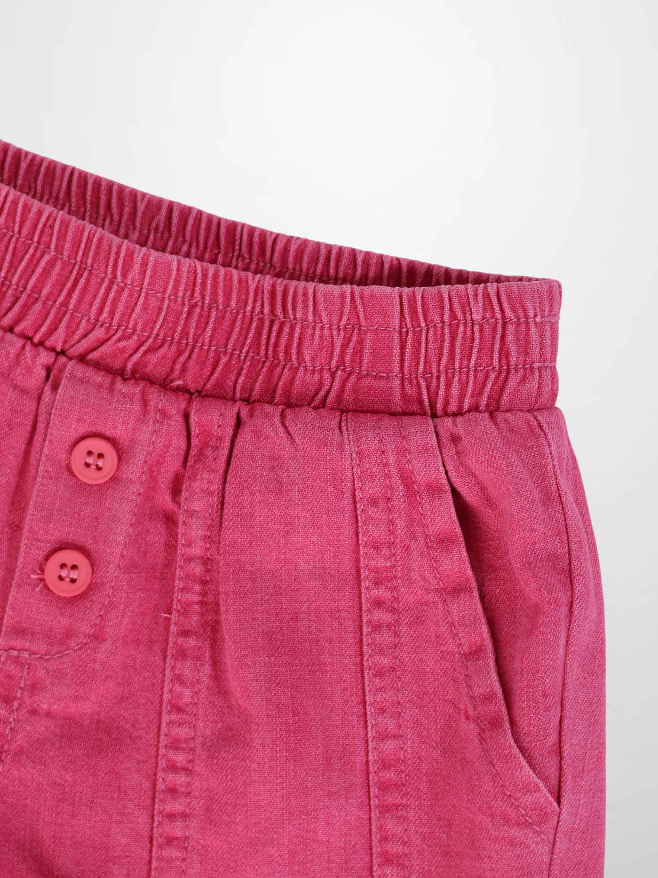 Paneled pink denim shorts with elastic waistband, front buttons, and side pocket.