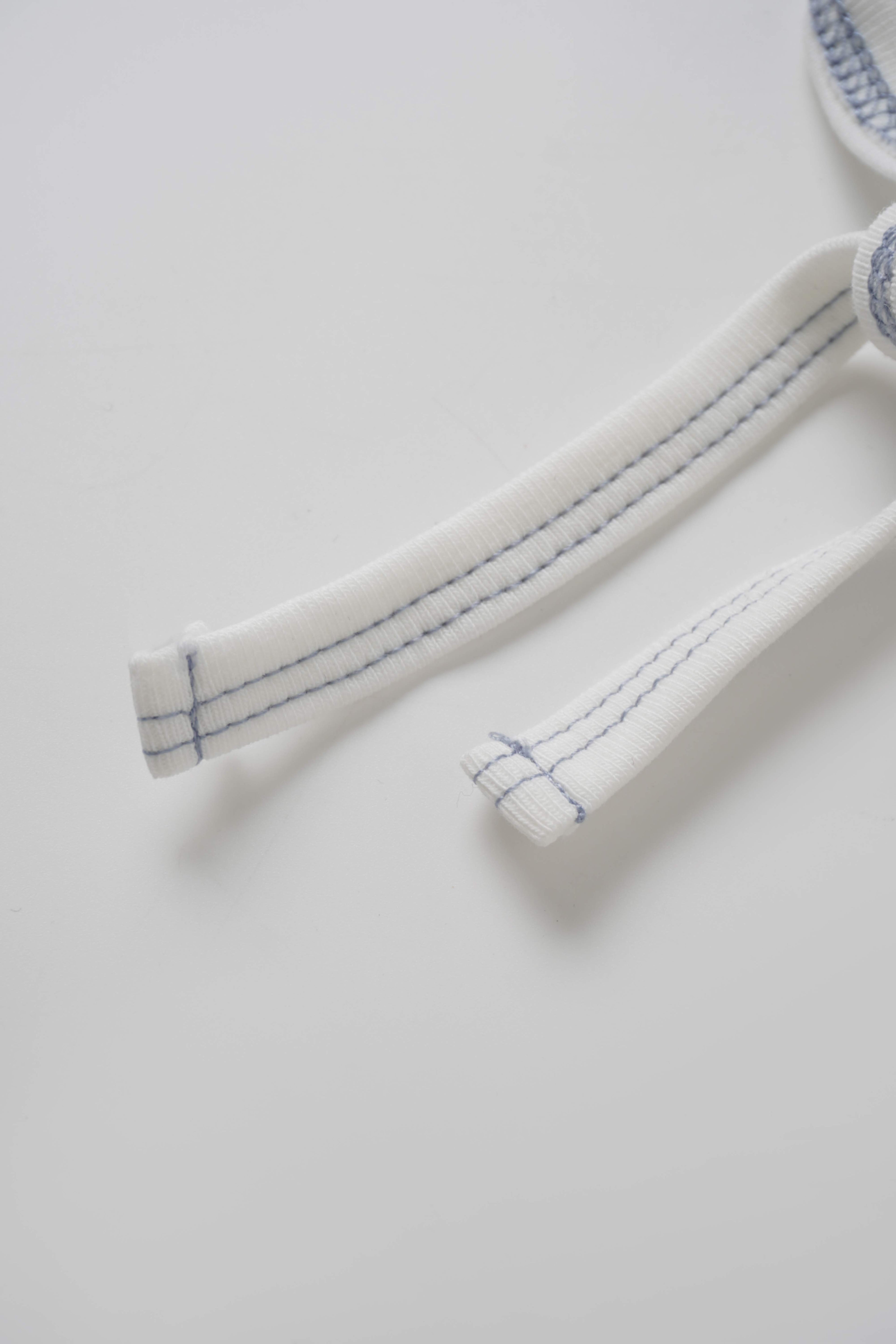 Mini Gallery Bonnet for boys, white fabric with blue stitching on the ties