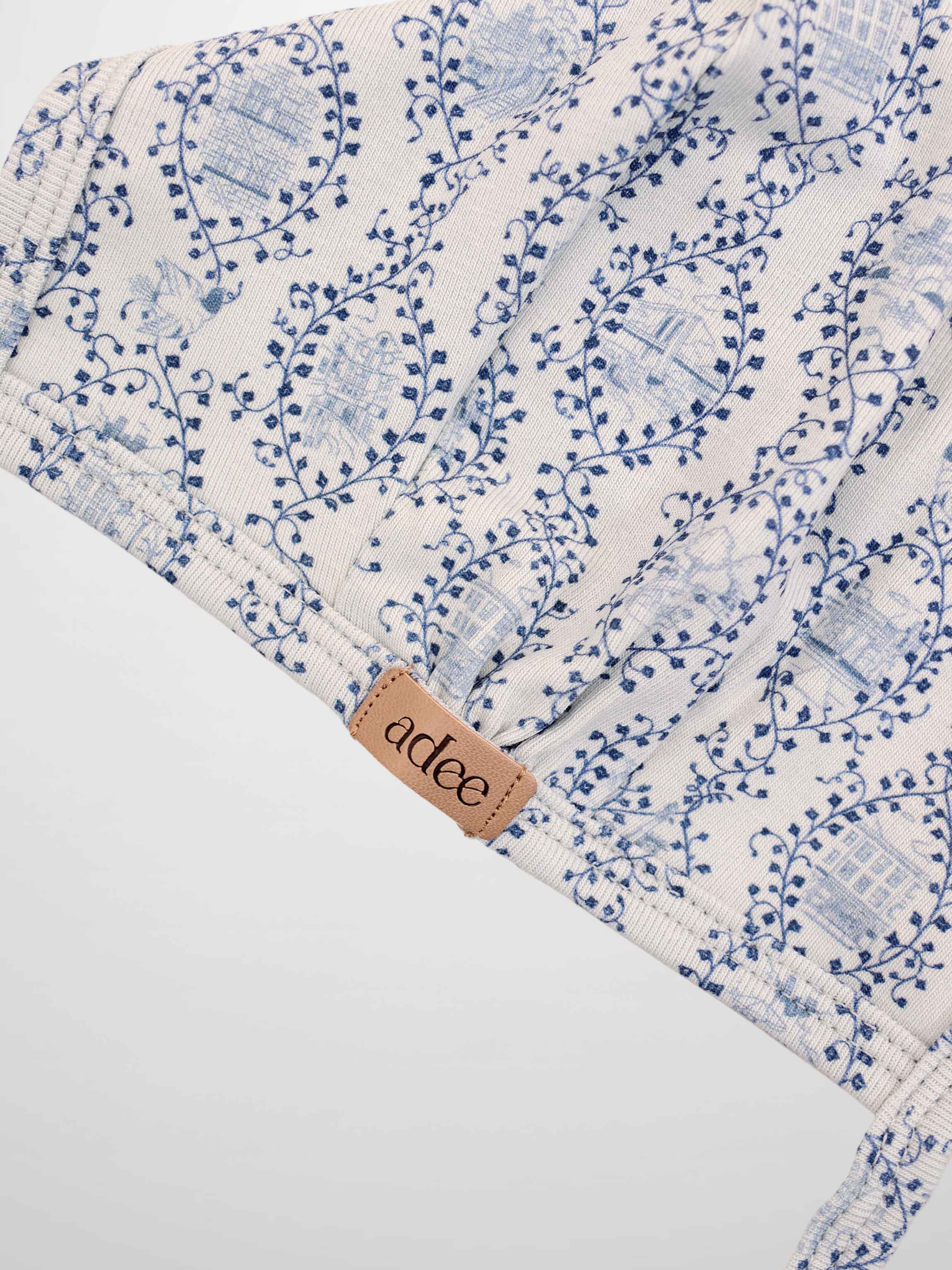 Blue Charm Bonnet for boys by Adee; cream fabric with dark blue vine pattern and tan brand tag.