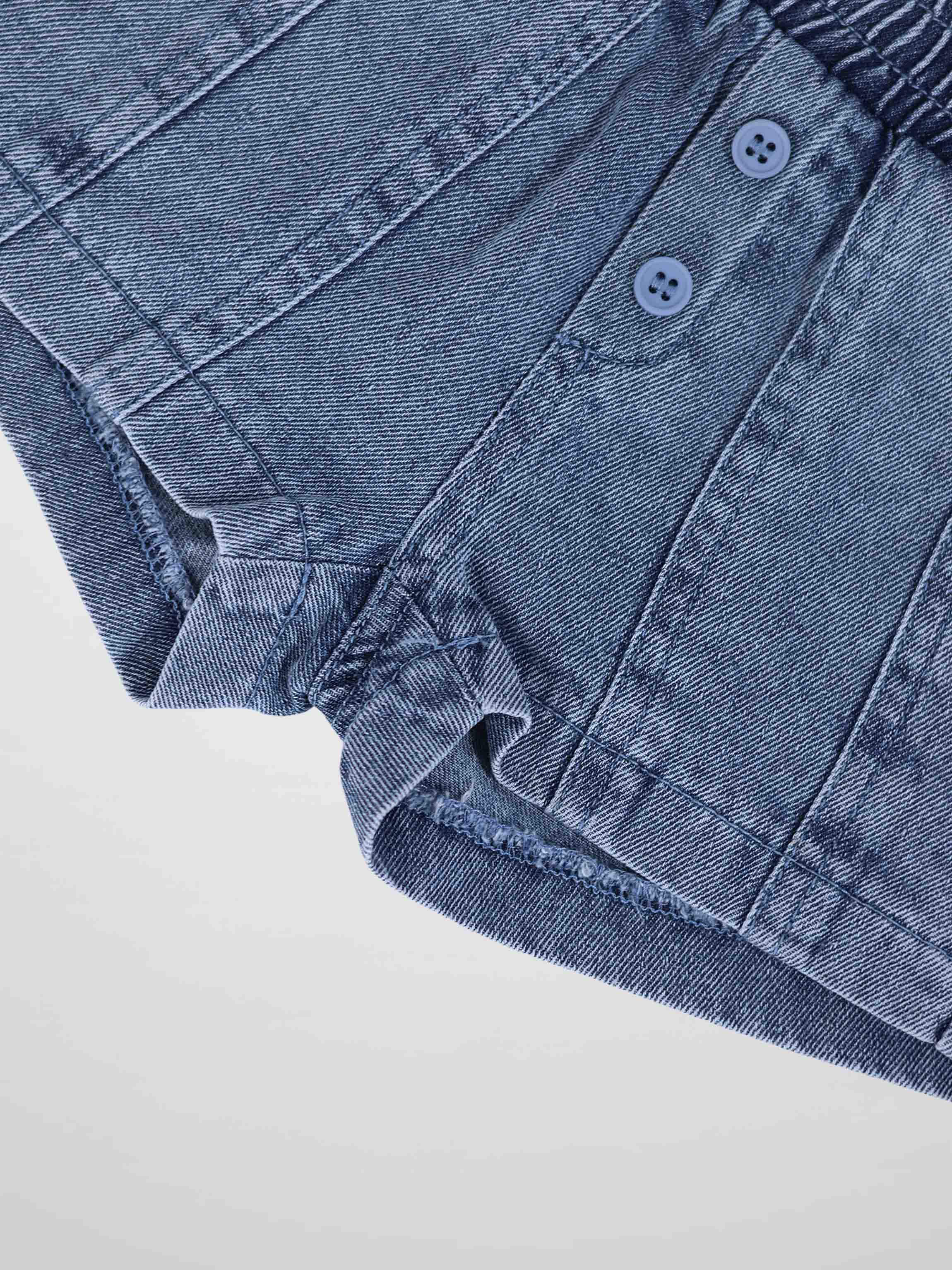 Paneled blue denim shorts with button front detail and rolled hem, close-up