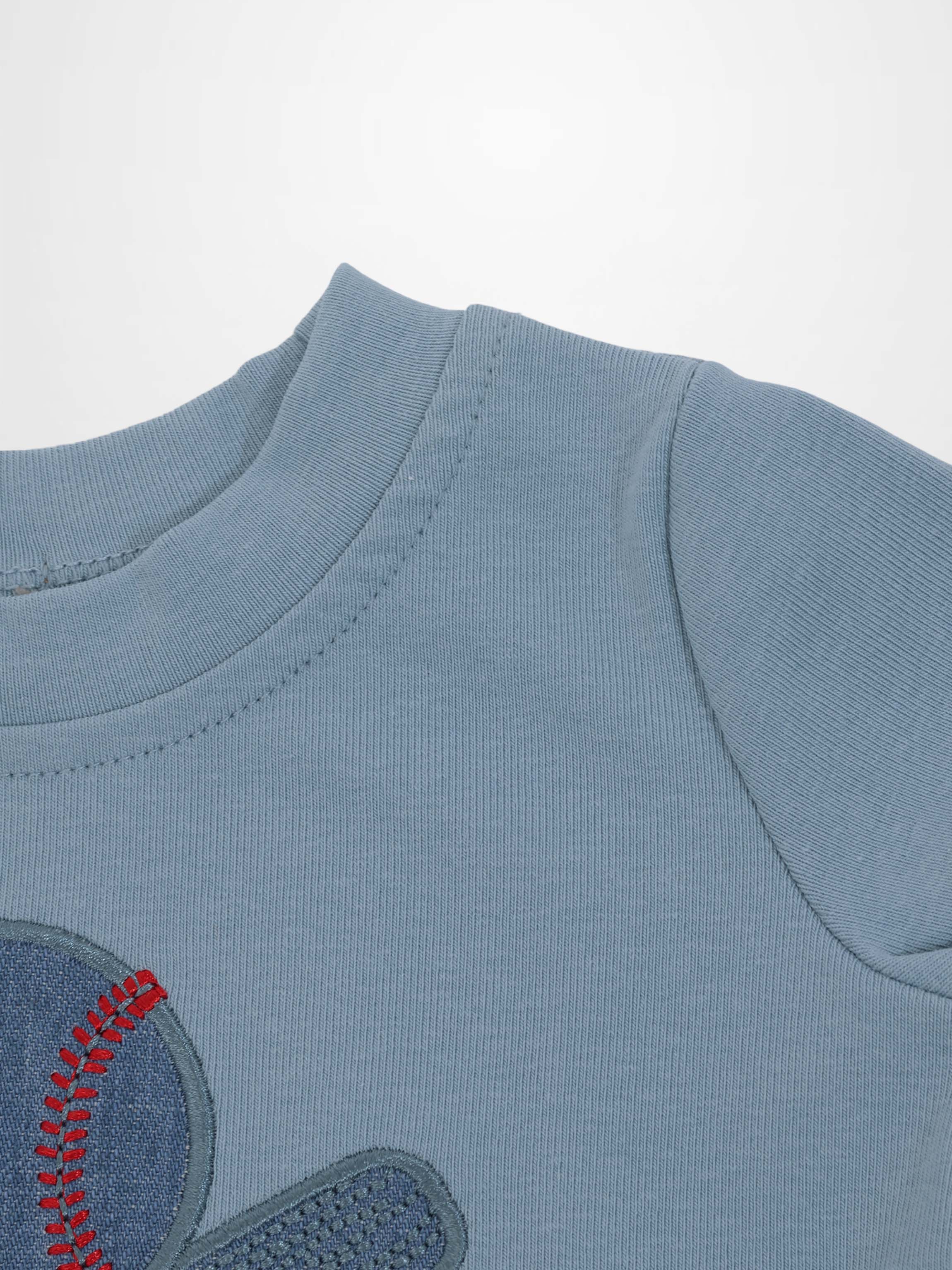 Light blue baseball T-shirt with an embroidered patch featuring red stitching.