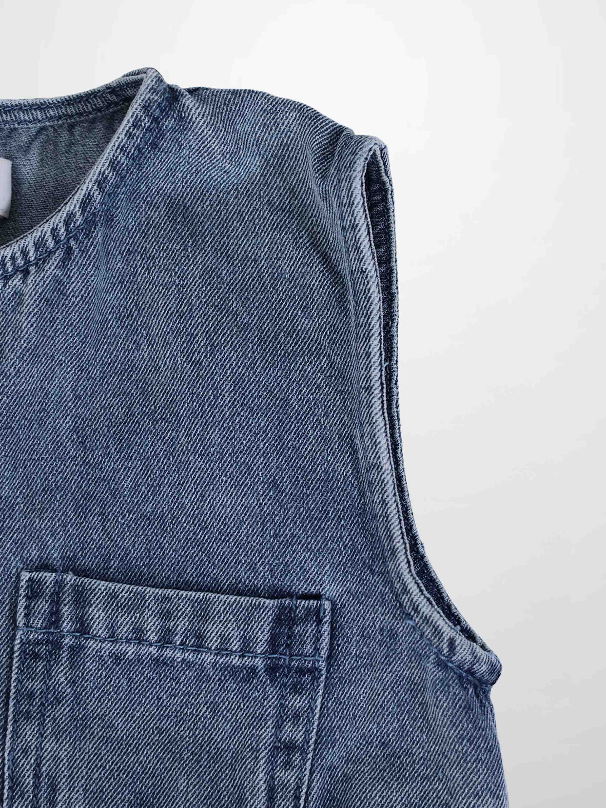 Blue denim romper with sleeveless top and front patch pocket, textured denim fabric.