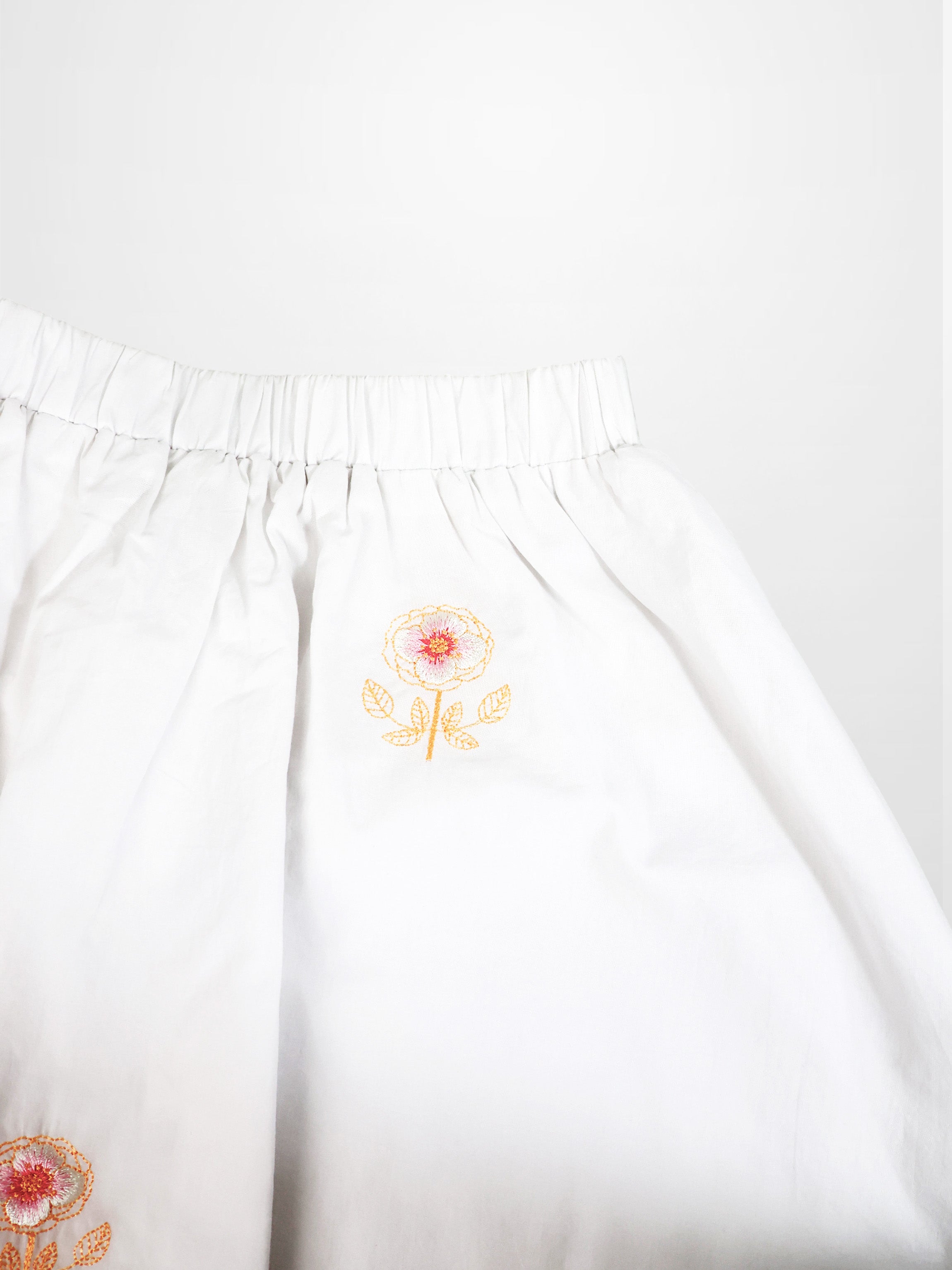 Adee Embroidered Flower Skirt for girls, white fabric with orange flower embroidery and elastic waistband.