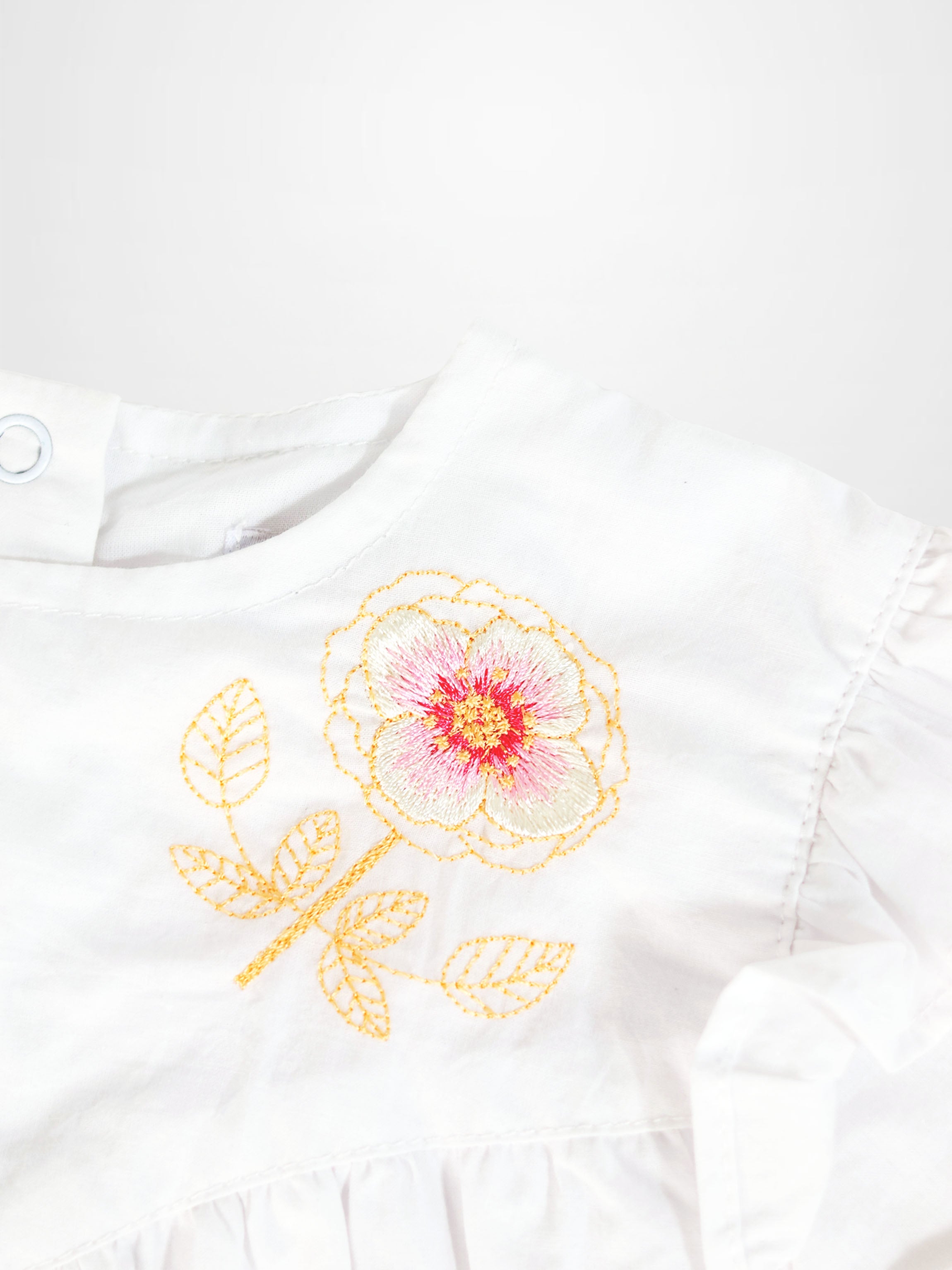 Embroidered flower romper, white fabric with yellow stems and leaves and pink-centered bloom.
