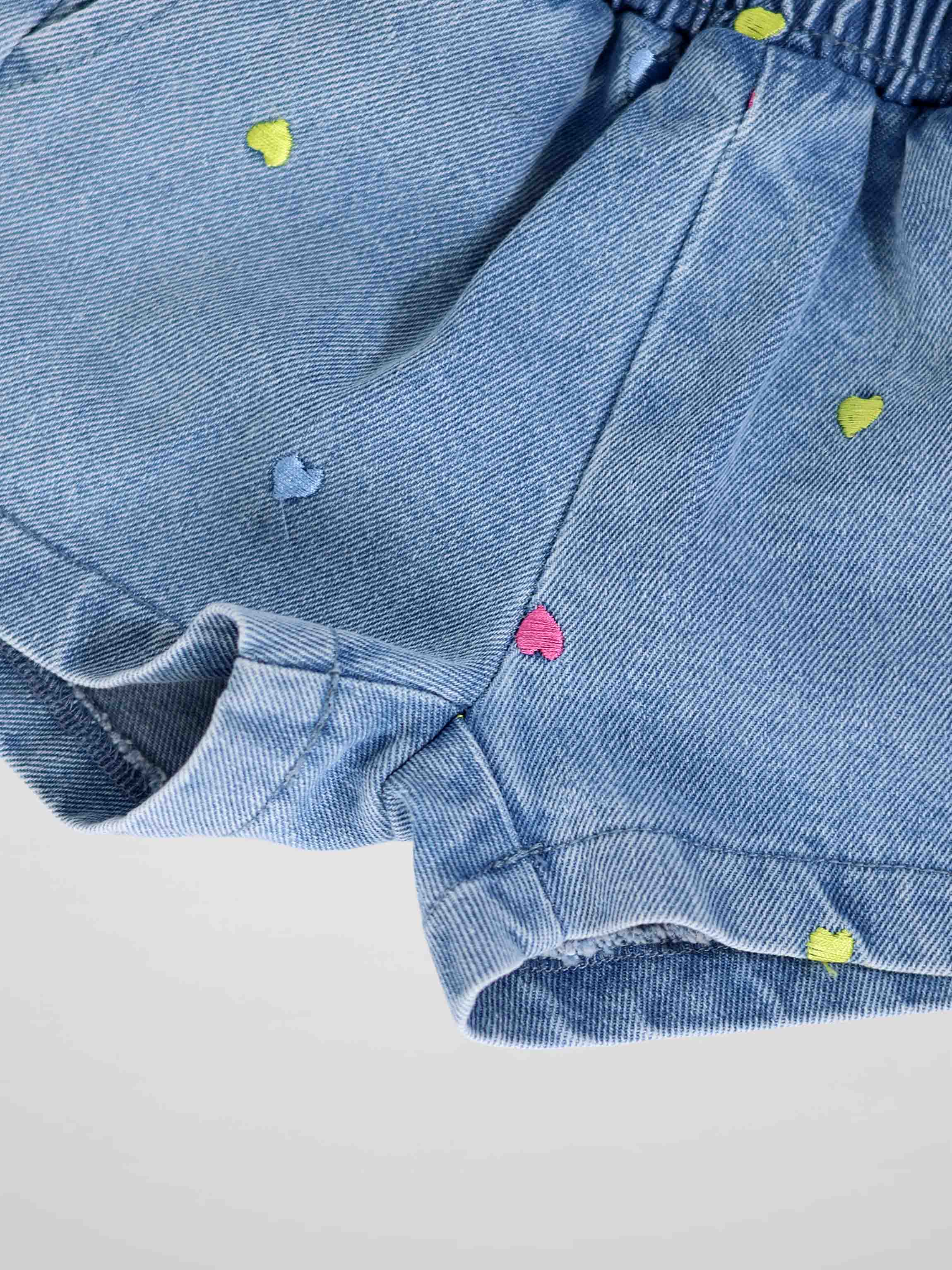 Light-wash denim shorts with multicolor heart embroidery and cuffed hems.