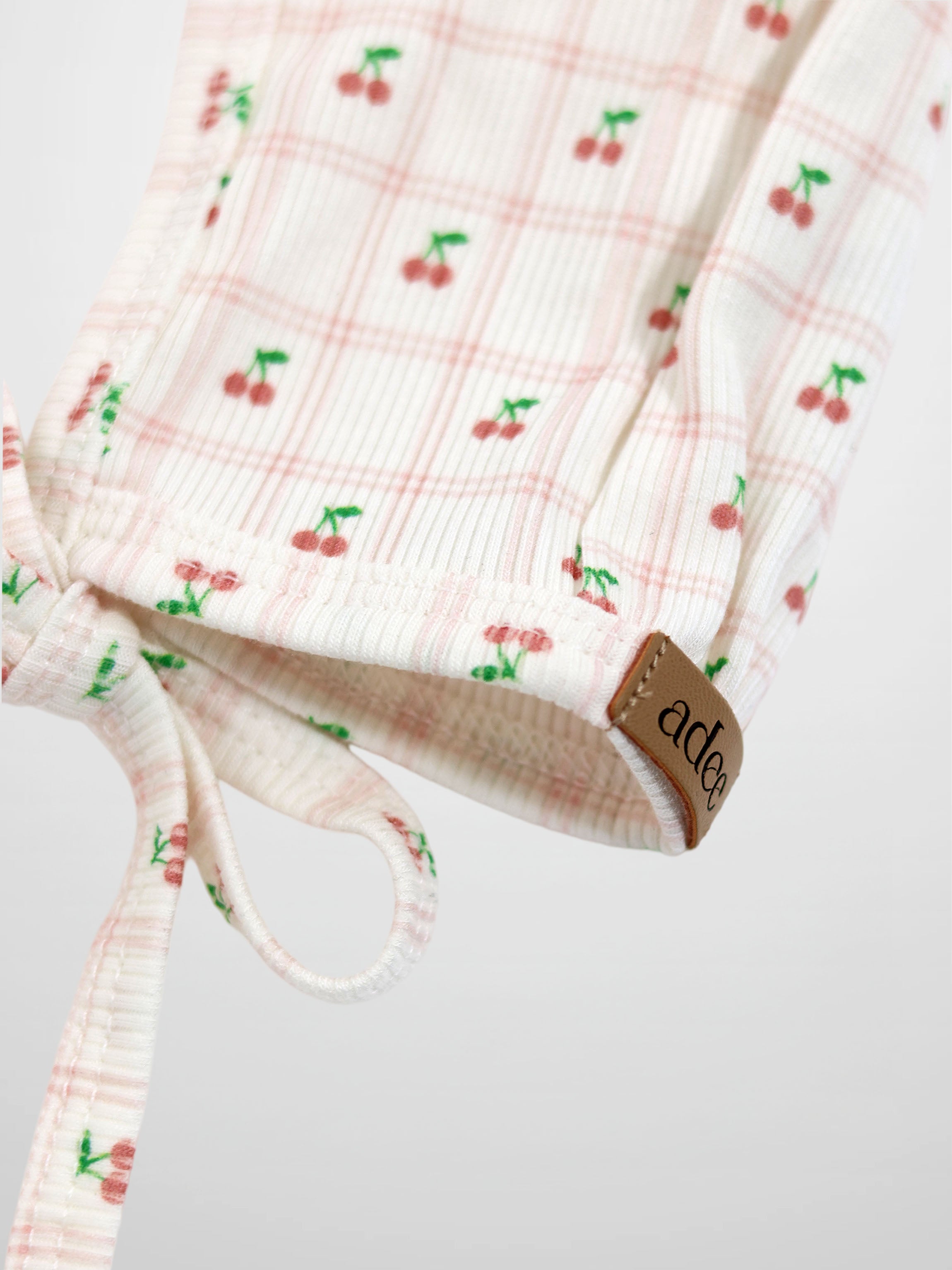 Cherry Window Bonnet for girls by Adee; light pink plaid with cherry prints, ribbed knit, tie closure