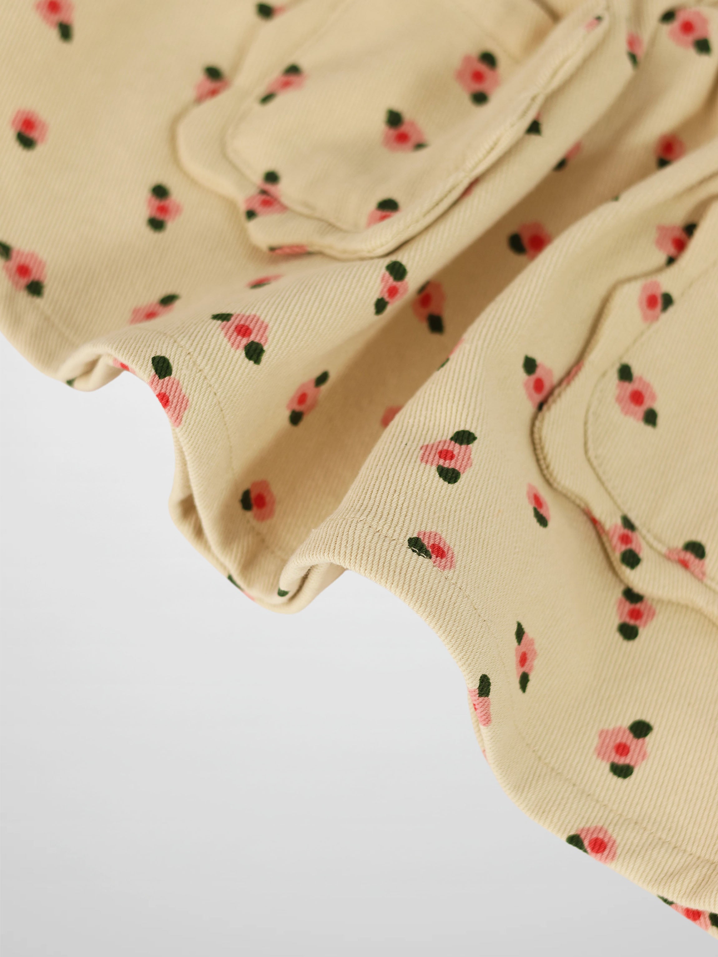 Tan floral skirt fabric with tiny pink blossoms and green leaves, close-up.