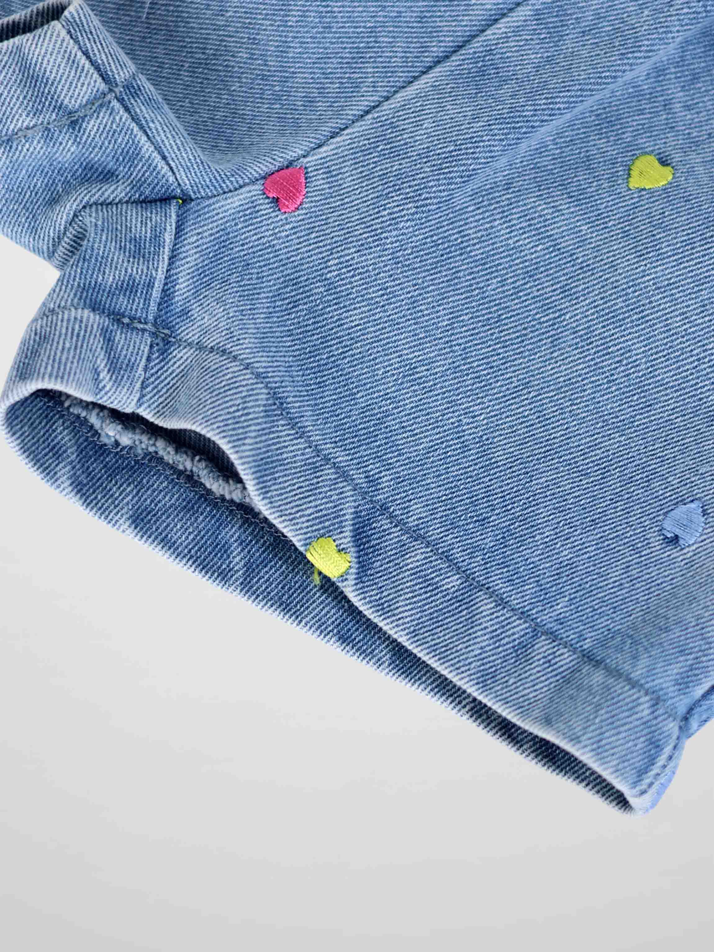 Close-up of light-wash denim shorts with colorful embroidered hearts scattered across fabric