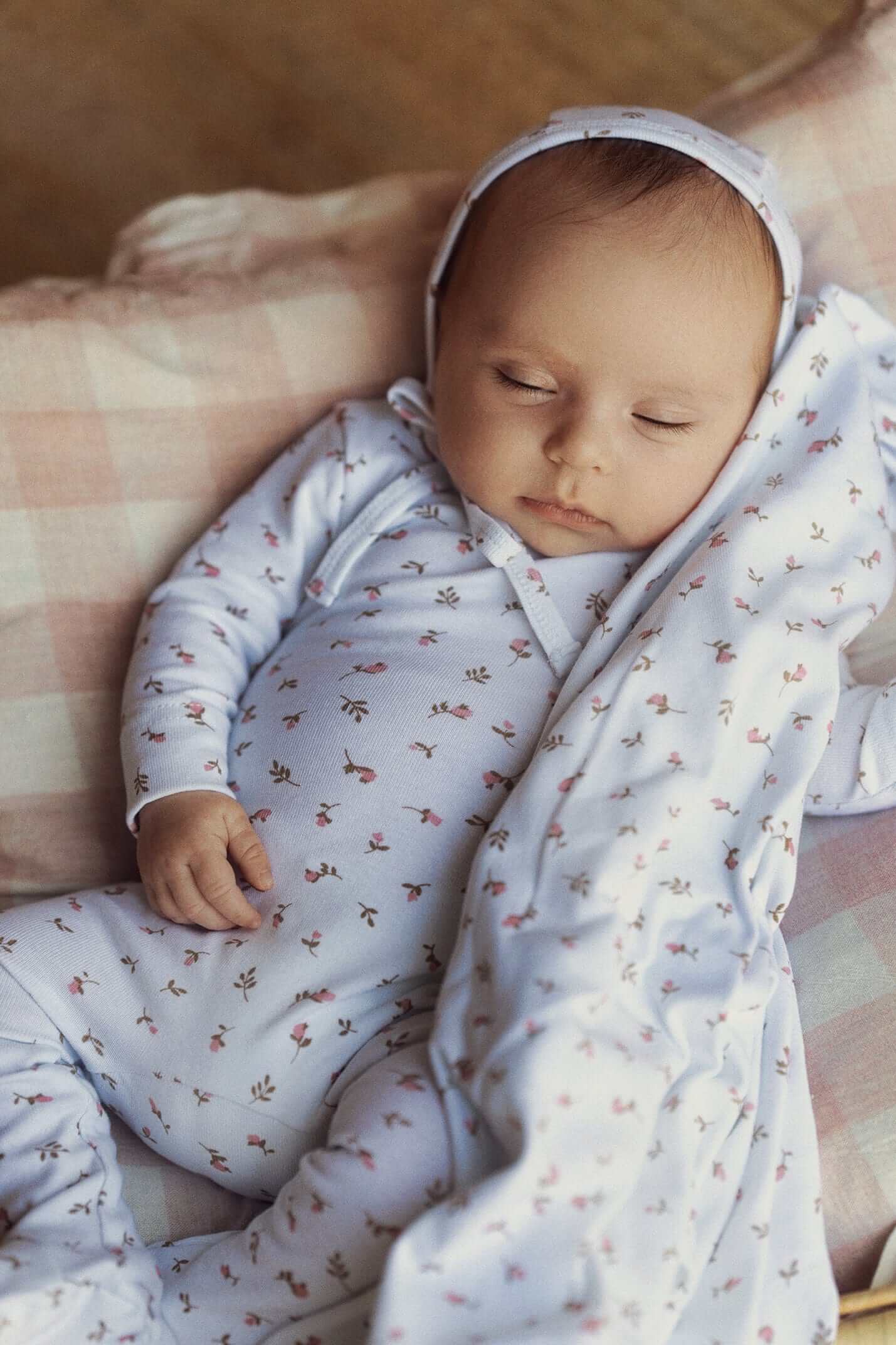 Baby in cozy flower jumpsuit , sleeping on soft blanket.
