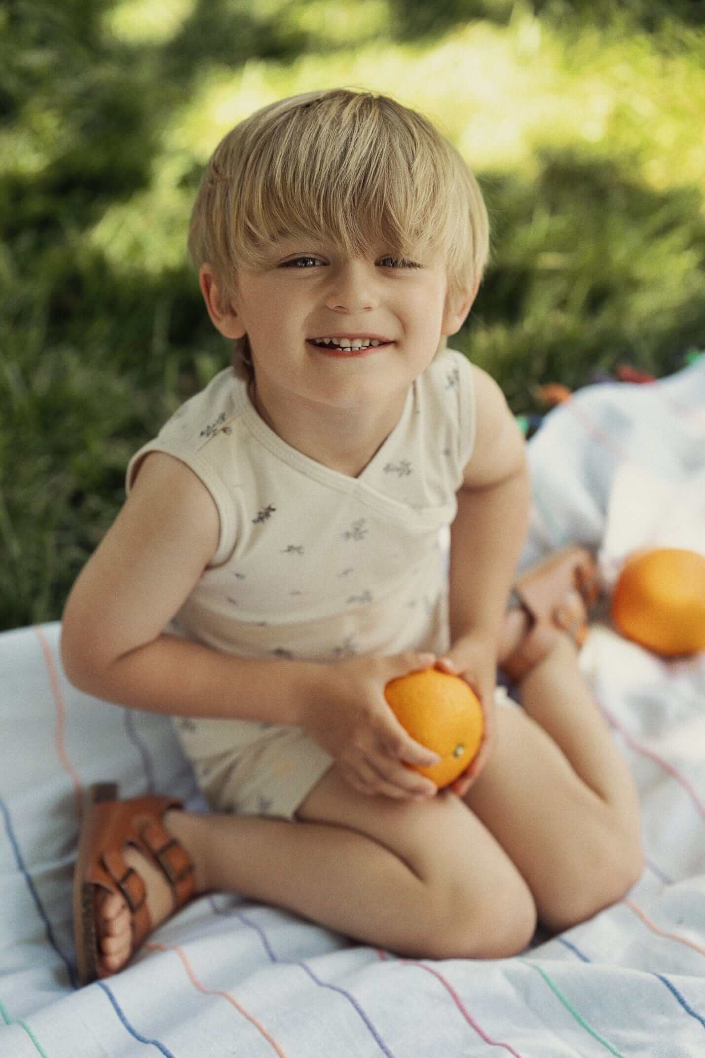Lilac Crossover Tank Set-Blue Little Boys Set; beige sleeveless top with small print, outdoors on a blanket.