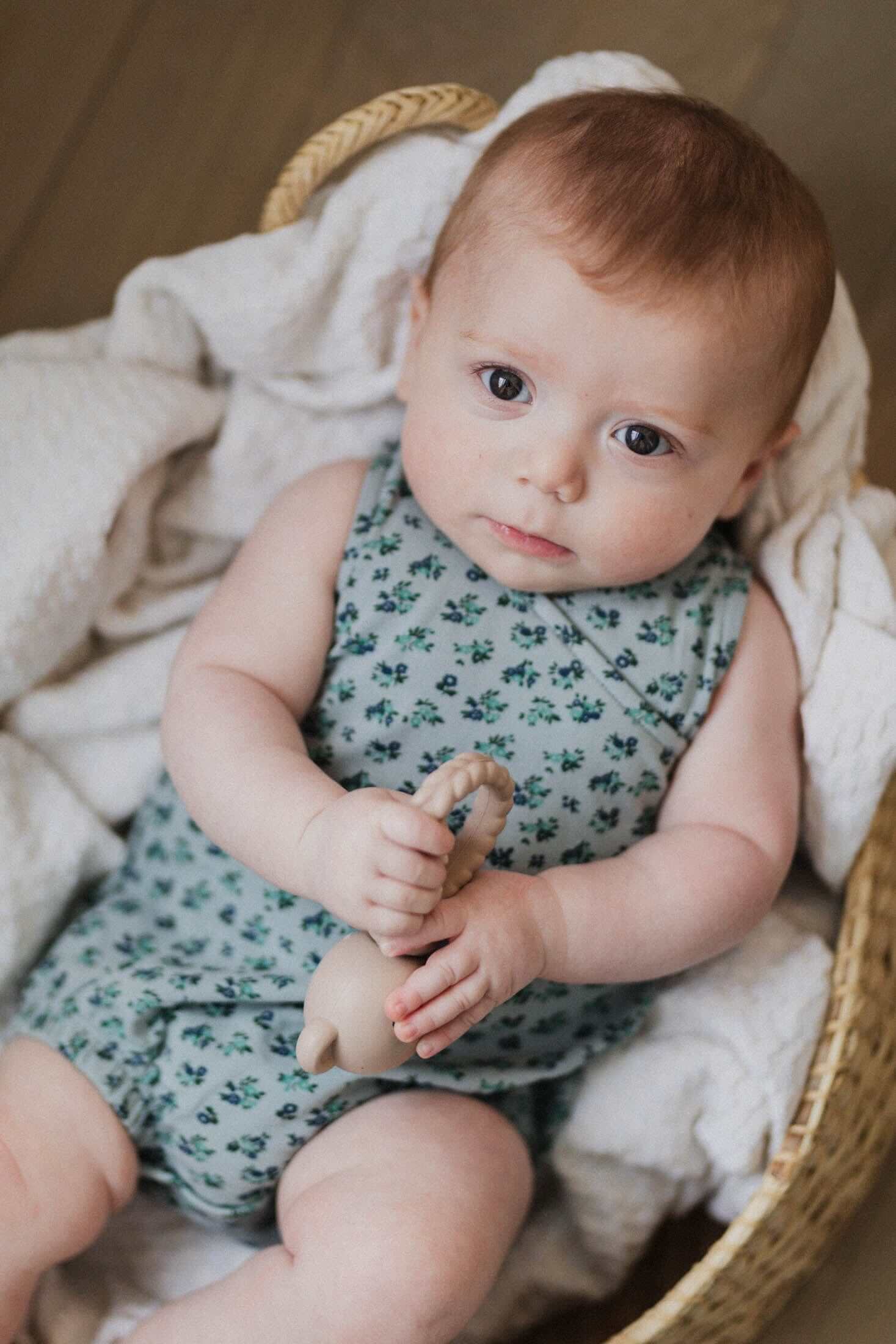 Infant in floral romper holding toy