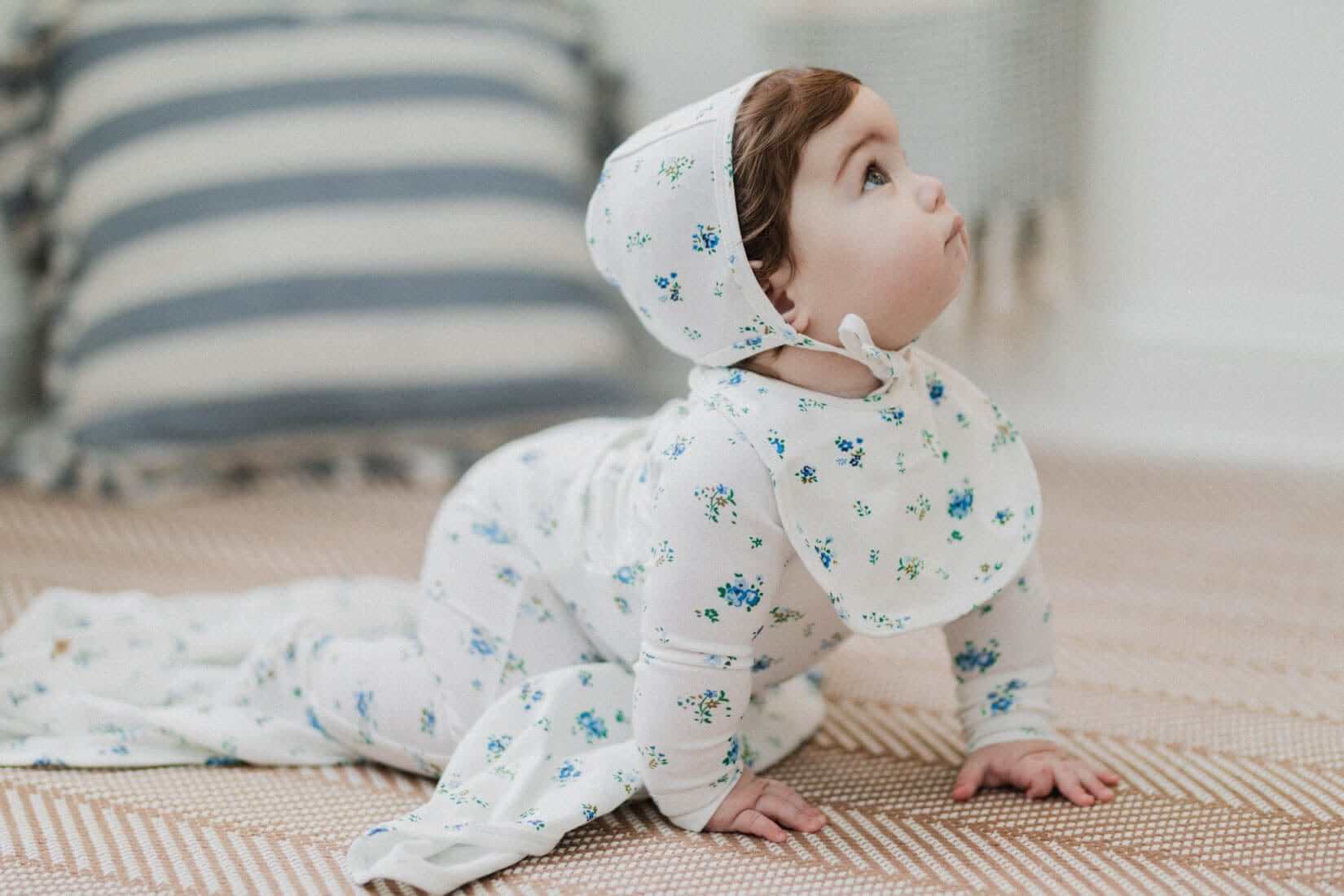 Baby boy in floral jumpsuit crawling on floor.