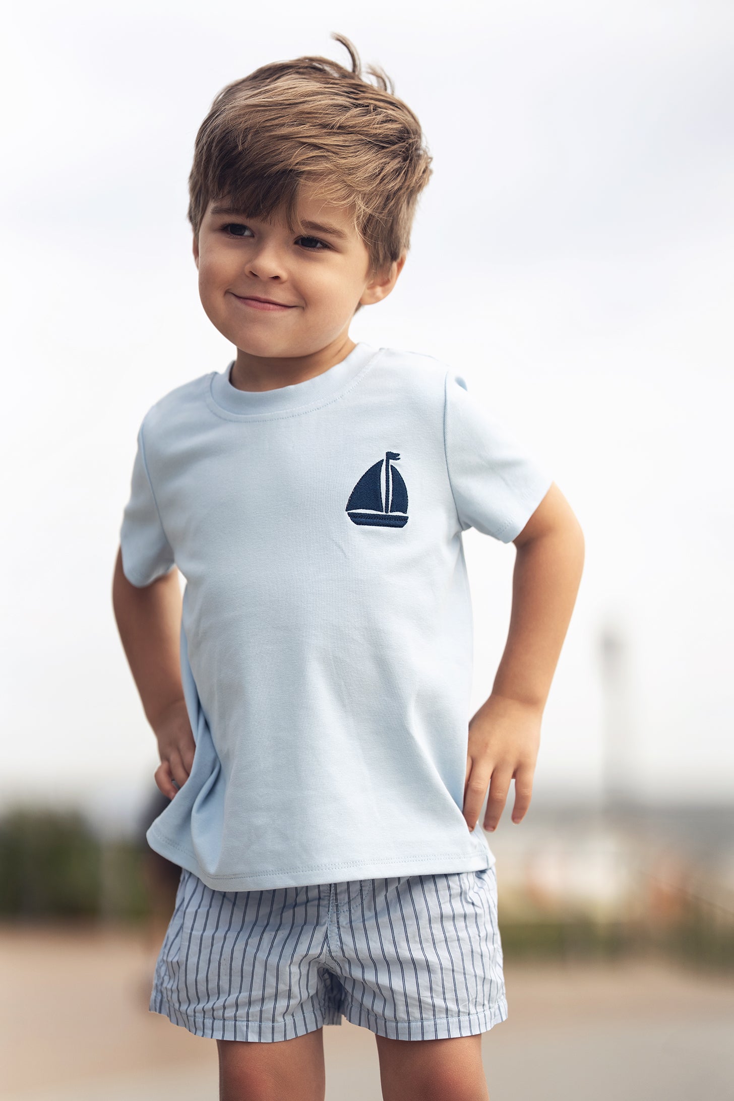 Little boy wearing light blue short-sleeve T-shirt with a navy sailboat emblem.
