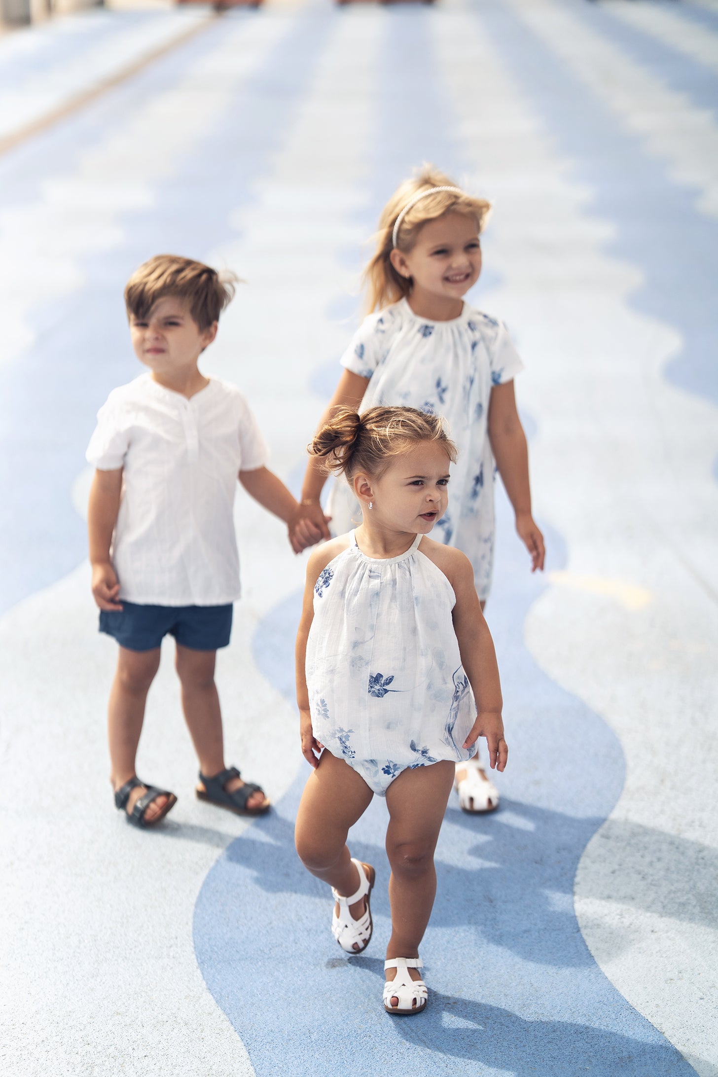 Three children in textured white cotton outfits walking on blue patterned surface.
