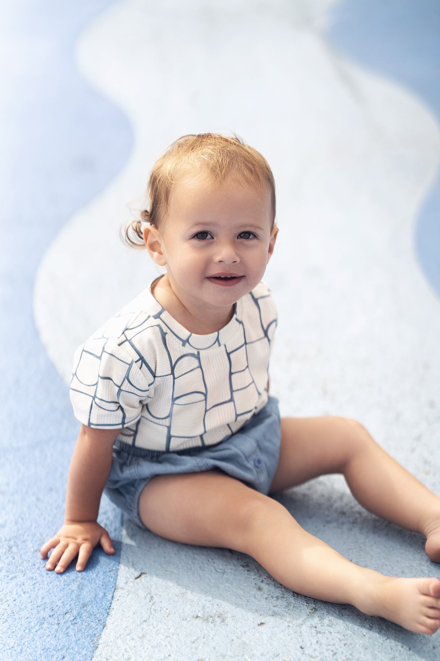 Abstract T-shirt with blue geometric pattern on a baby boy sitting on a blue rug.
