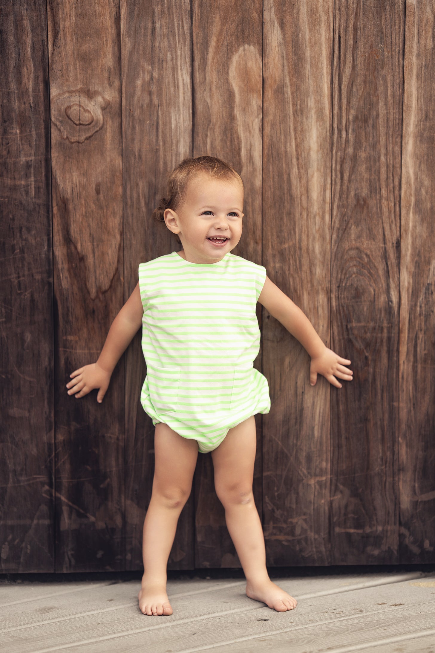 Neon Green Striped Romper on smiling toddler against wooden backdrop