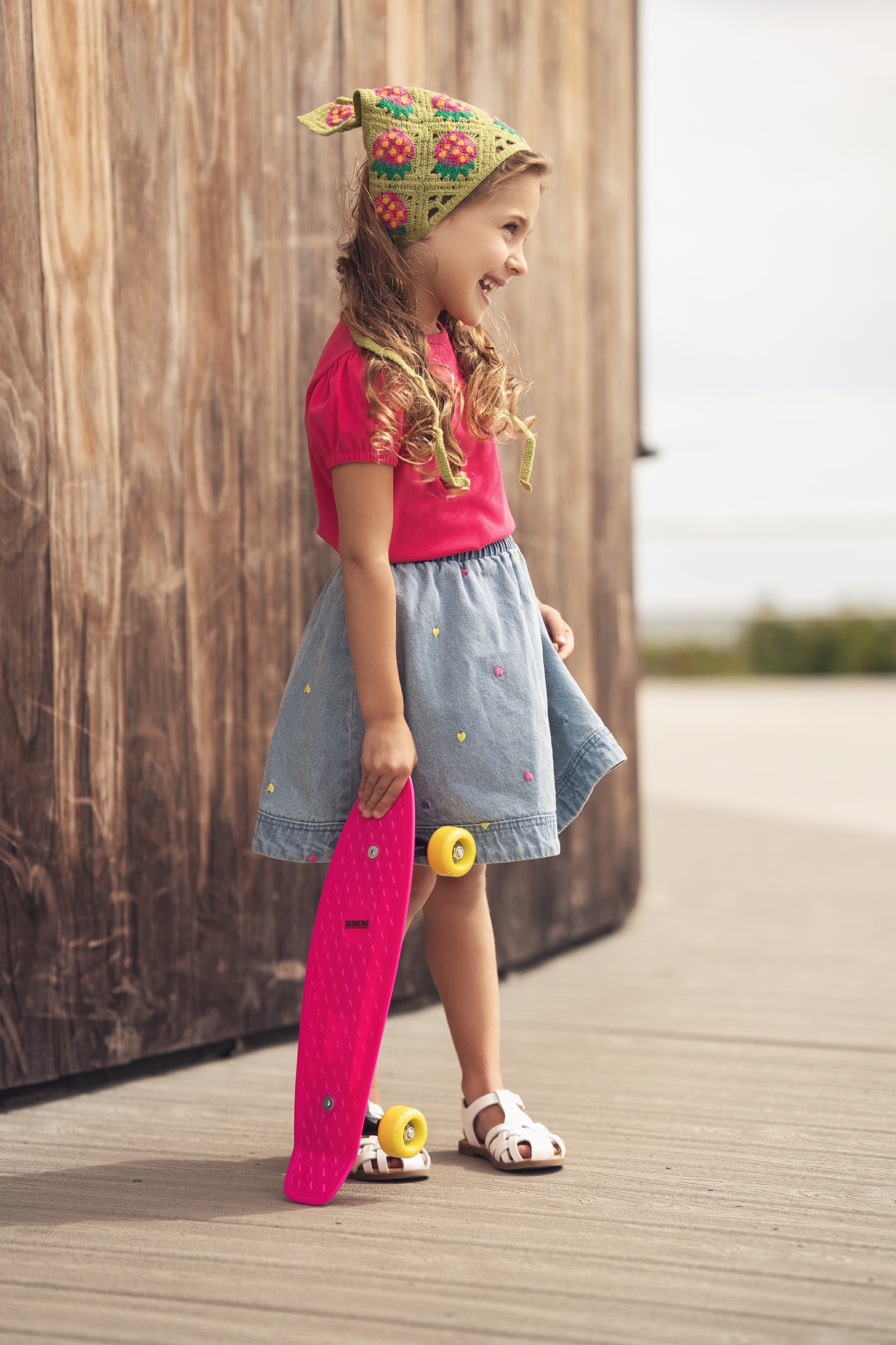 Adee girls pink short-sleeve bubble T-shirt worn by a smiling girl on a boardwalk with a pink skateboard
