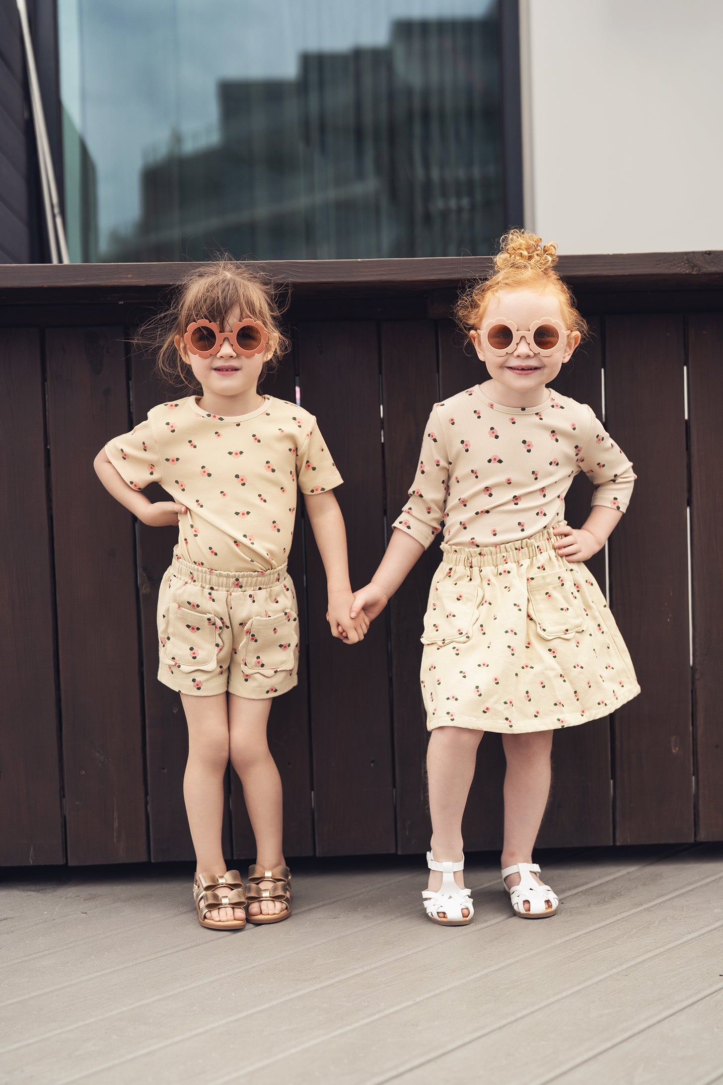 Tan Floral Shorts: two young girls in beige floral outfits, one wearing shorts and the other a skirt, holding hands.