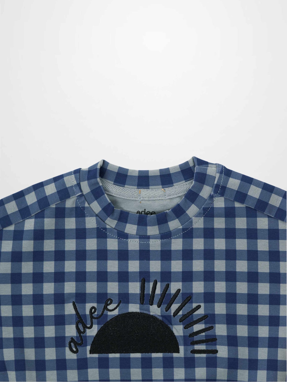 Blue gingham pajama top with black sun embroidery on the front.