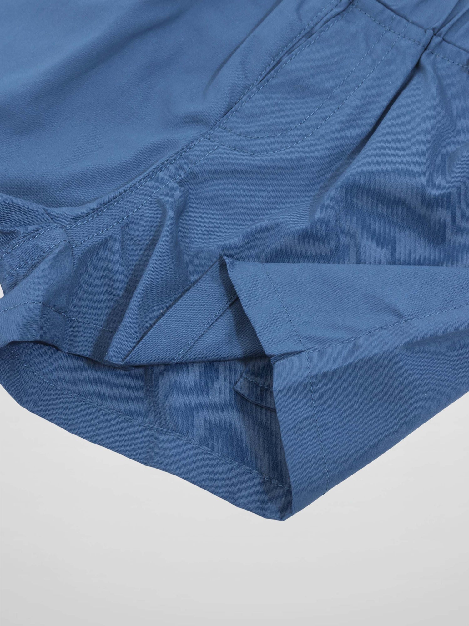 Blue cotton shorts with a curved side pocket and visible stitching.