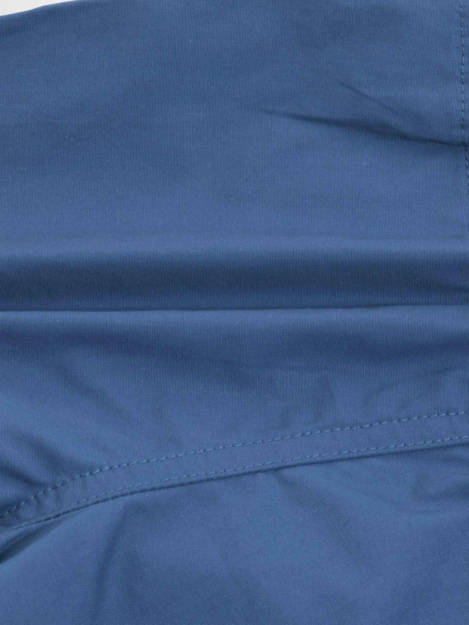 Blue cotton shorts fabric close-up with visible stitching and seam.