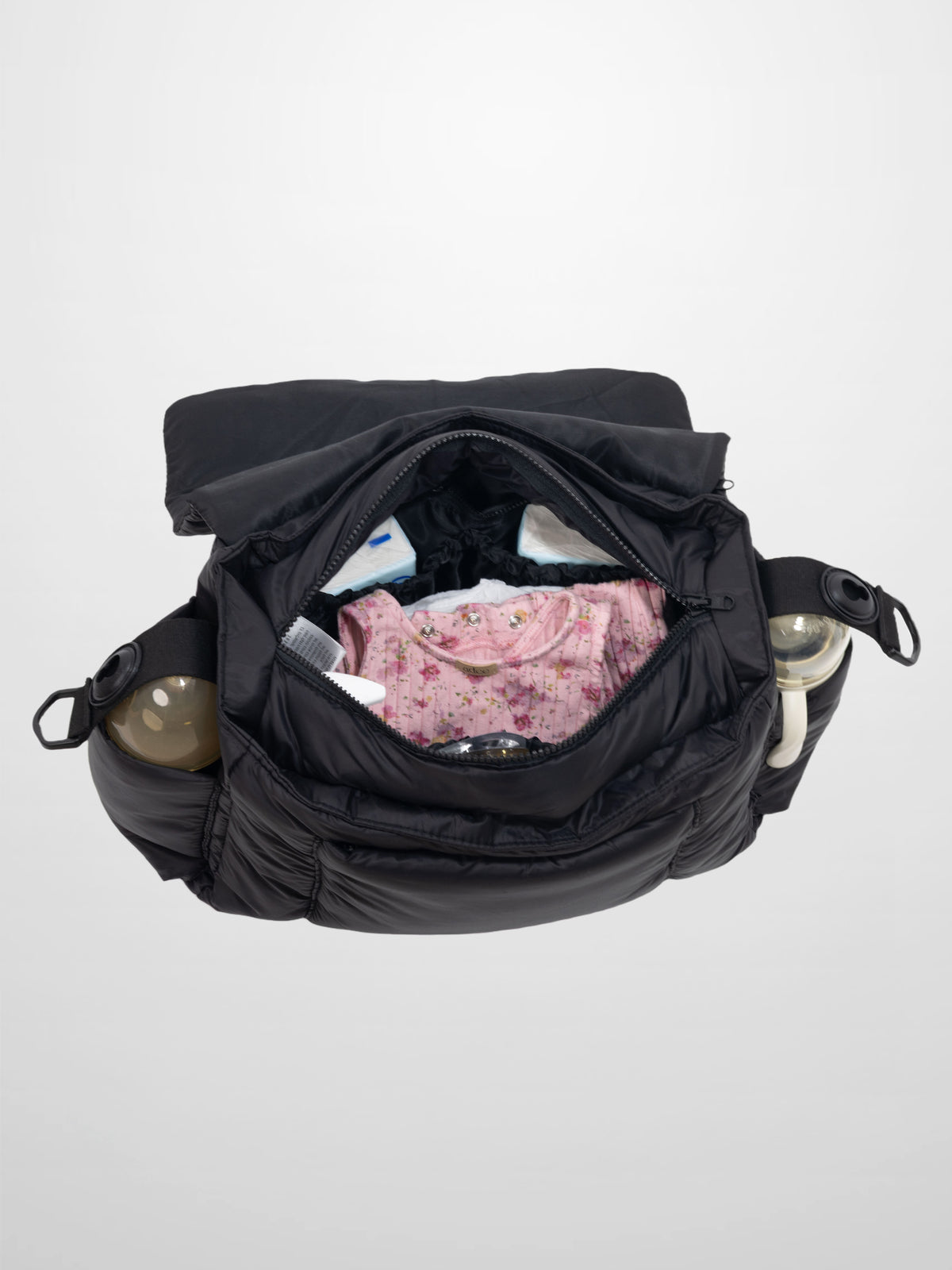 Black padded diaper bag with foldover flap, open to show pink floral baby clothes and side bottle pockets.