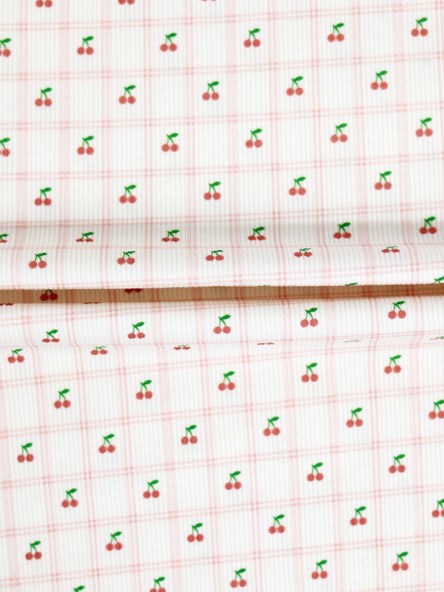 Adee Cherry Window Stretchy girls fabric with tiny red cherries and green stems on a pale pink windowpane grid