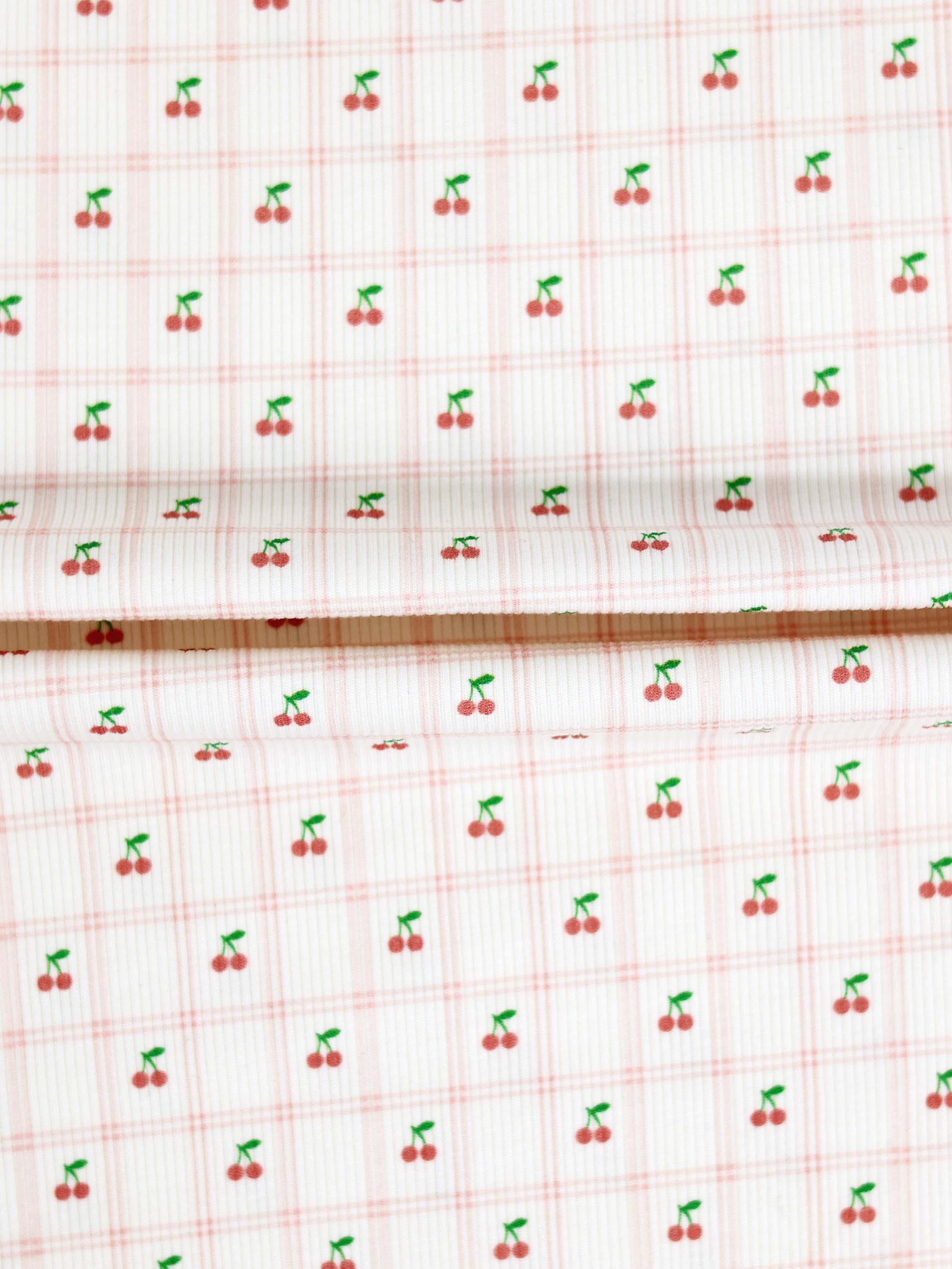 Adee Cherry Window Stretchy girls fabric with tiny red cherries and green stems on a pale pink windowpane grid