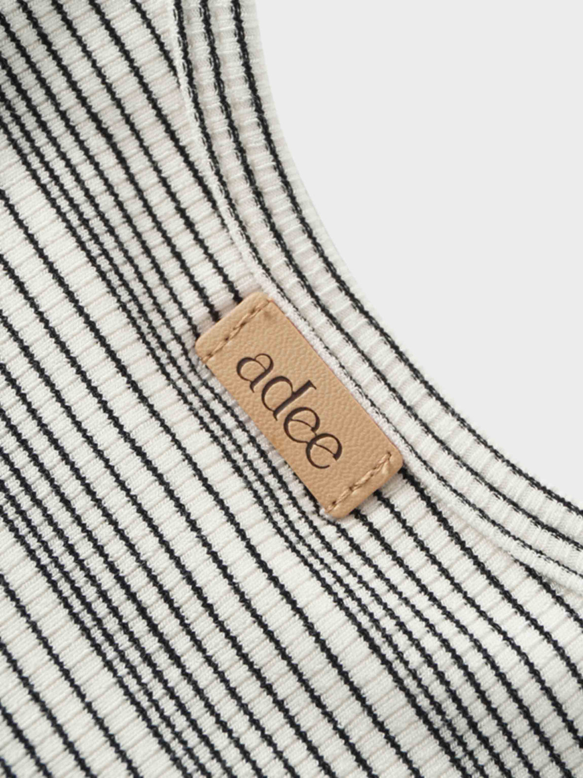 Textured white fabric with soft feel and thin black stripes in a fitted 3/4 sleeve T-shirt, tan leather tag.