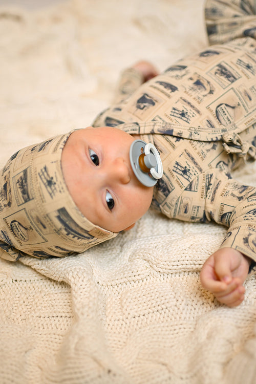 cute baby boy with a pacifier wearing a jumpsuit with printed vintage stamps