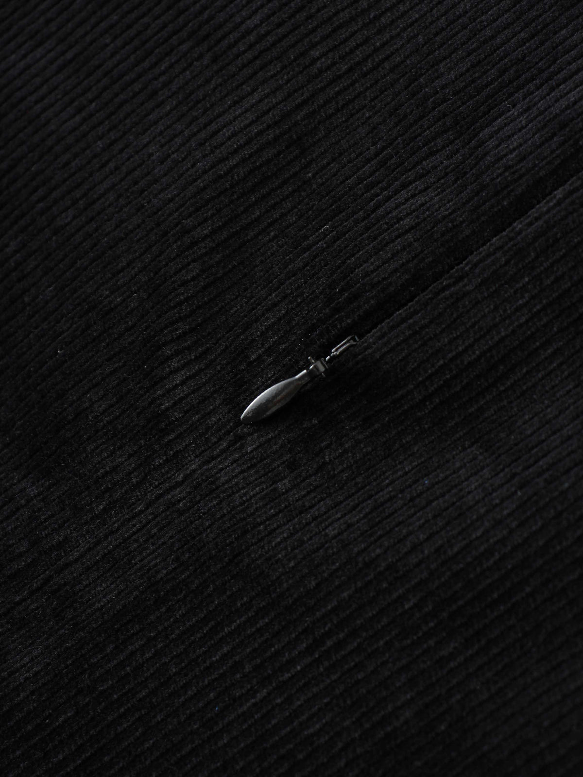 Close-up of black corduroy fabric with a metal zipper pull.
