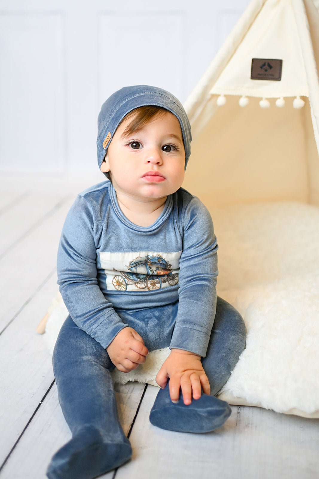 Velour Carriage Stretchy blue boys outfit by Adee, plush velour with wagon graphic on the chest, worn by a baby.