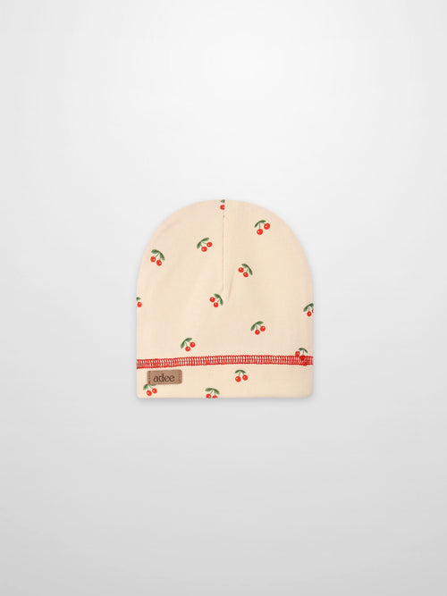 Red Cherry Hat for girls; beige knit beanie by Adee with scattered cherries and red stitching.