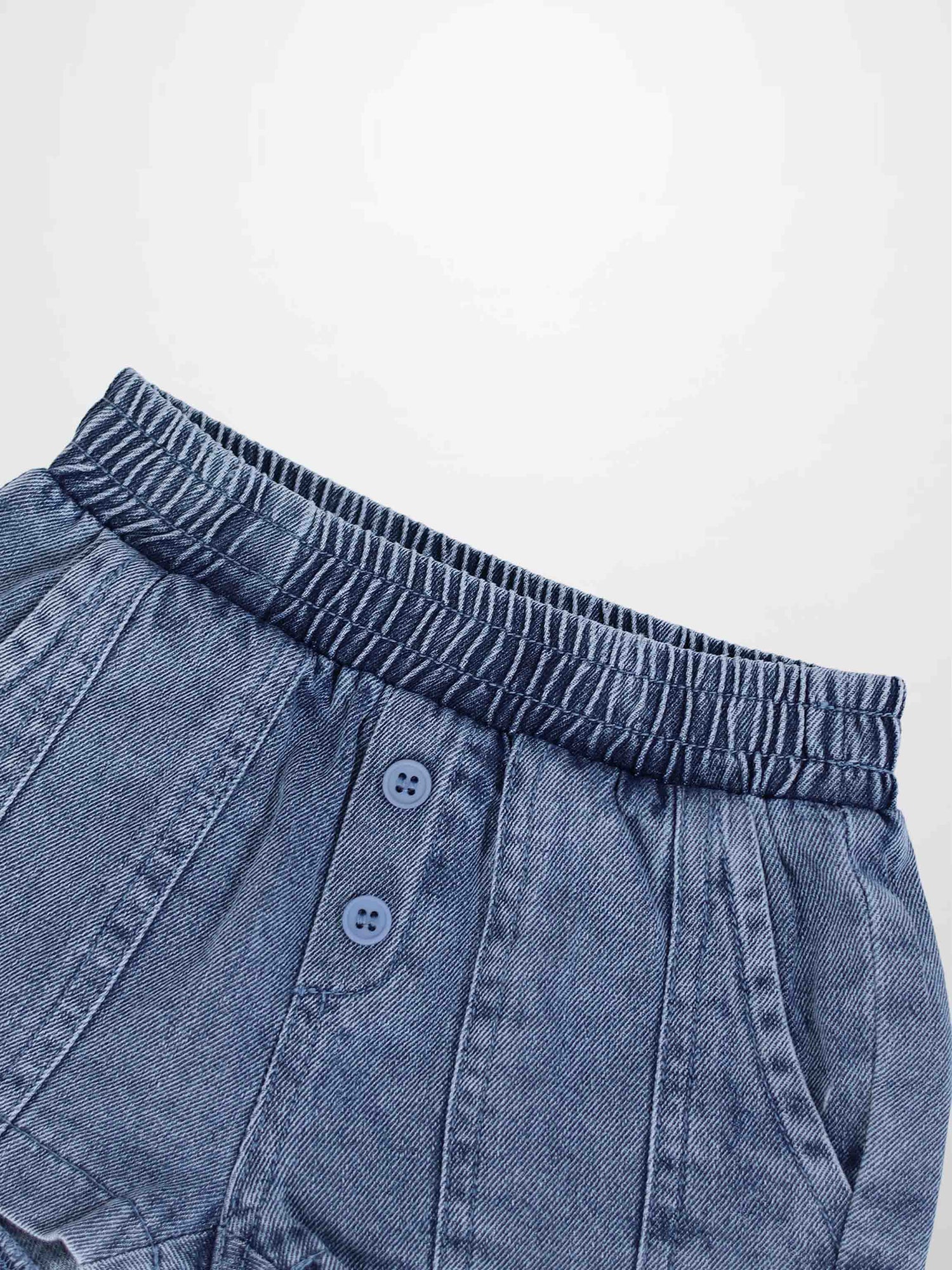 Paneled blue denim shorts with elastic waistband, front button placket, and side pockets.