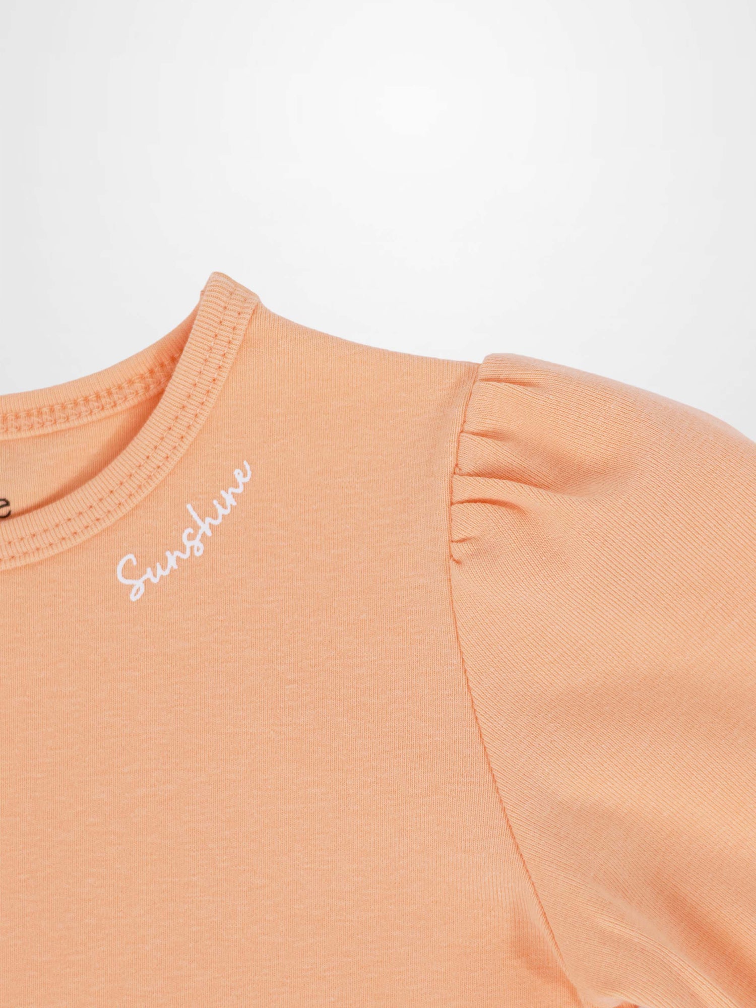 Short puff sleeve peach T-shirt close-up with white Sunshine script near the neckline.