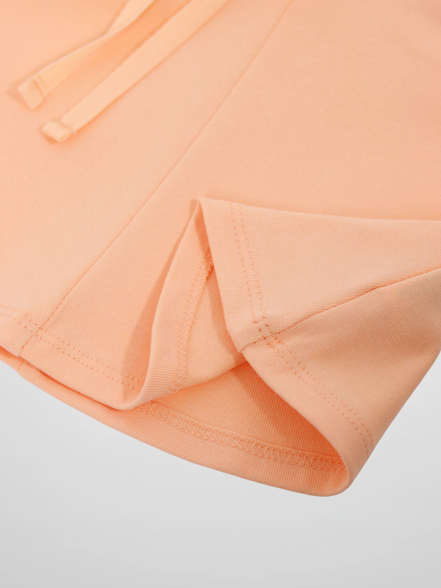 Adee 6 Panel Skirt for girls in peach, close-up of peach fabric, visible stitched hem and waistband drawstrings.