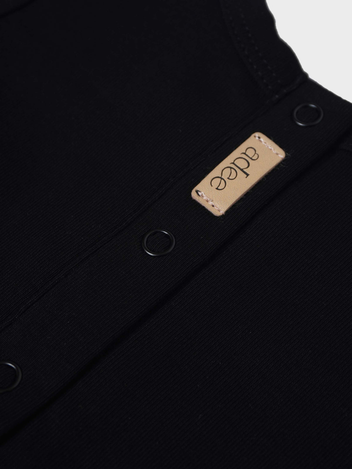 City Stretchy - Black unisex footed jumpsuit by Adee with beige brand patch.