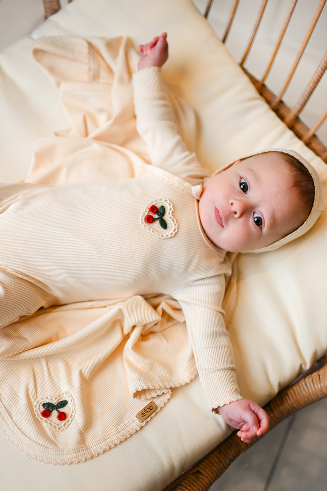 baby girl wearing a jumpsuit with cherry icon with bonnet hat and a blanket