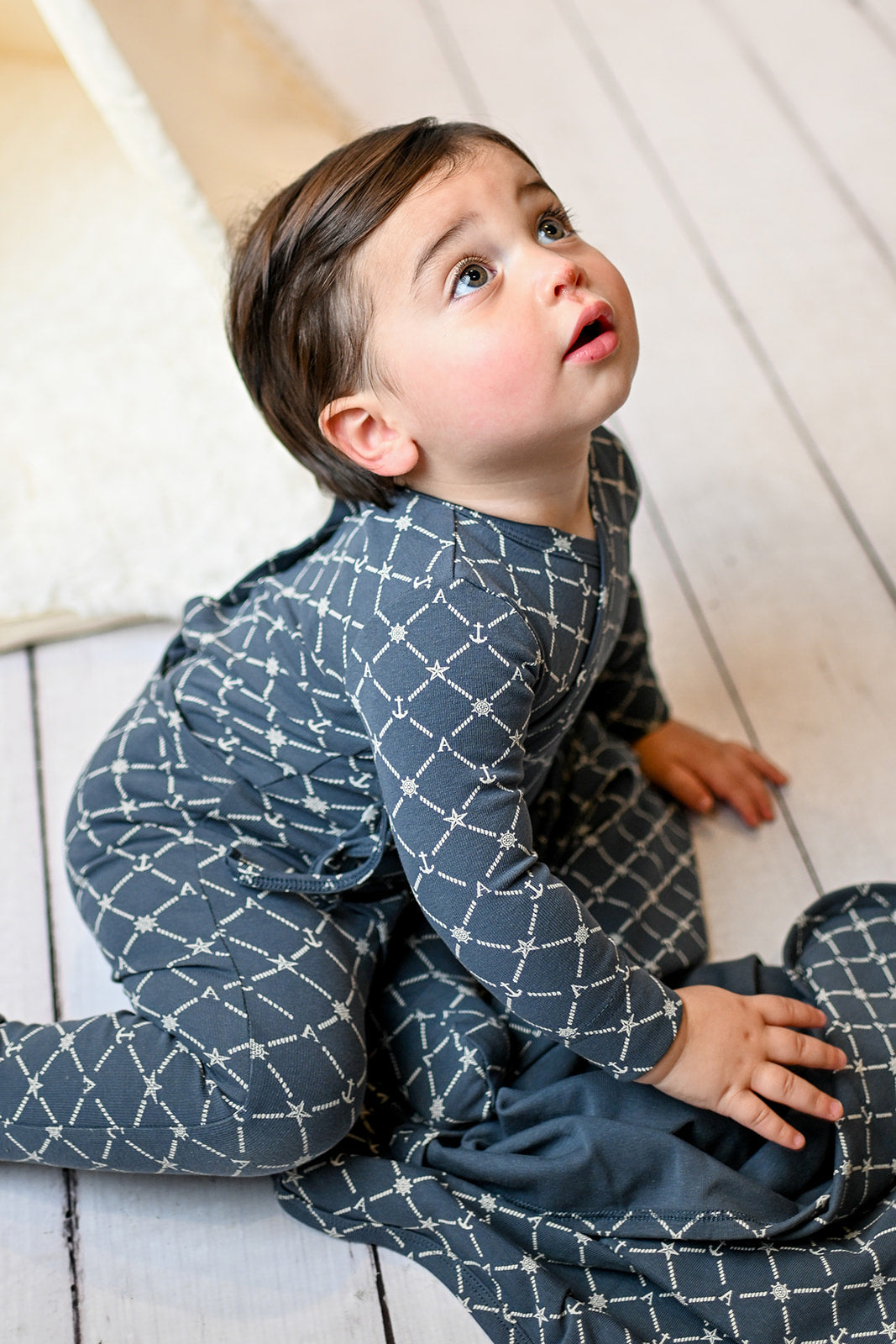 Baby in navy crossover jumpsuit with side tie, diamond rope pattern and anchor and star accents.