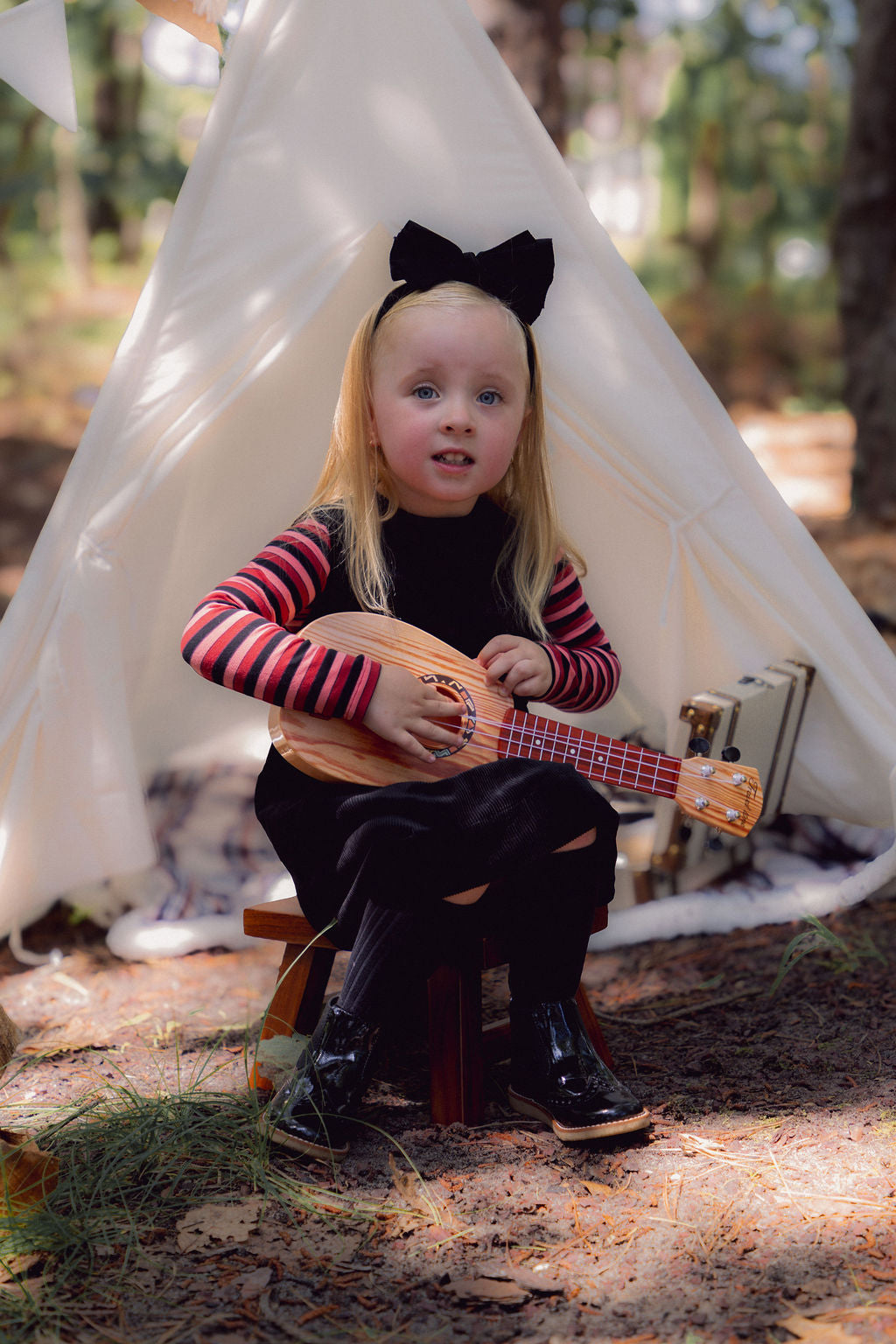 Corduroy jumper - black worn by a child outdoors, A-line with round neckline, patch pockets, playing a ukulele.