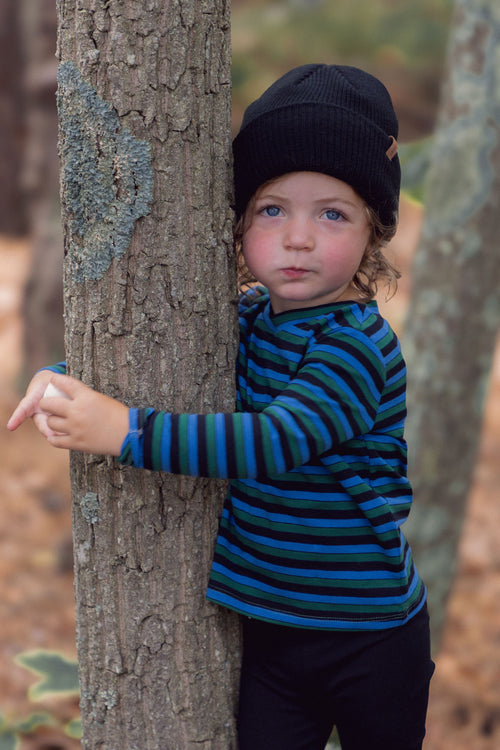 Child wearing blue striped long-sleeve crew-neck T-shirt with green and black stripes, hugging a tree outdoors.