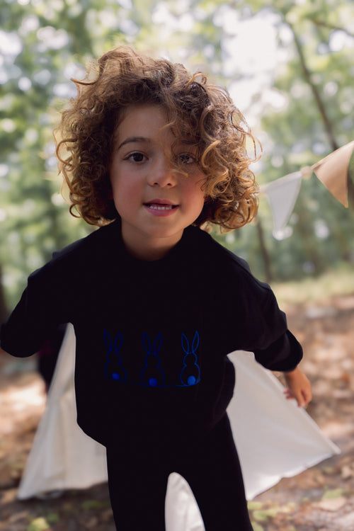 Child wearing black sweatshirt with blue embroidered bunnies outdoors.