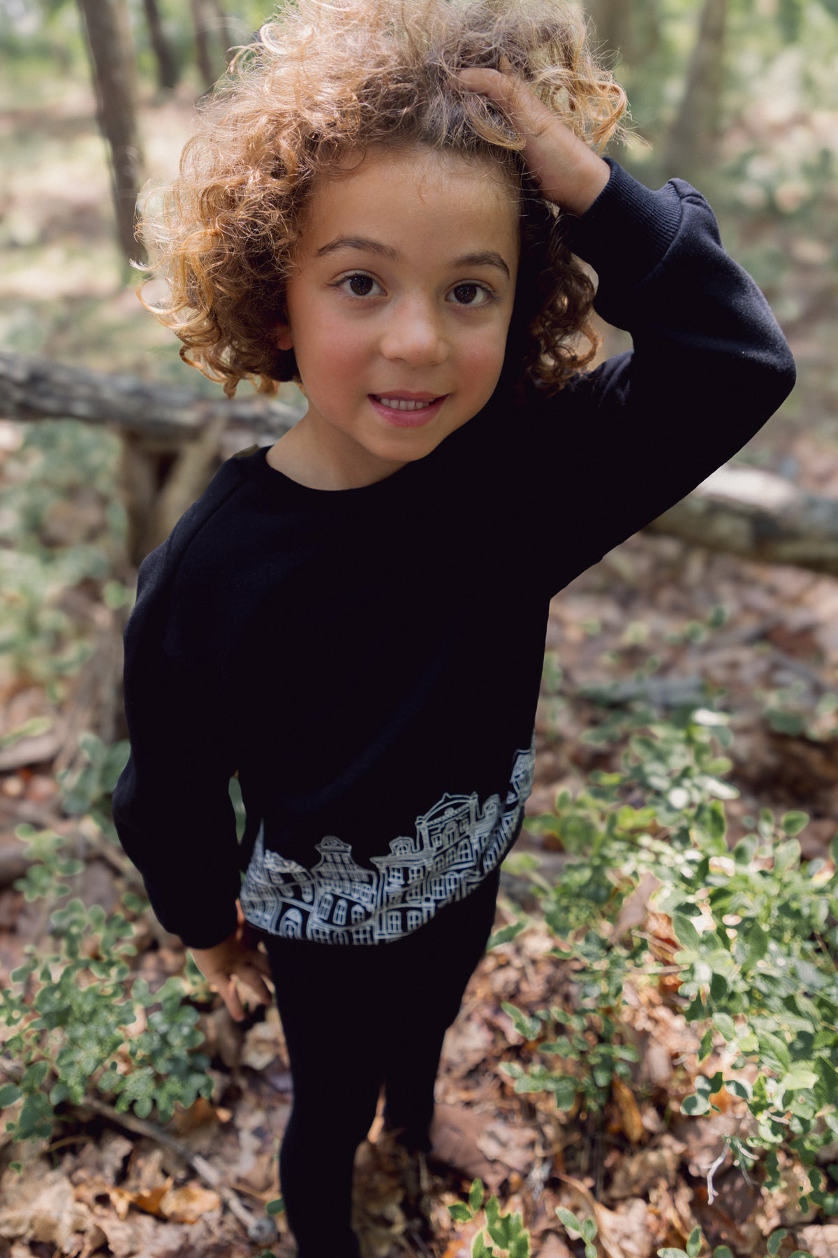 Child wearing a black Skyline Sweatshirt with white cityscape graphic in a forest setting.